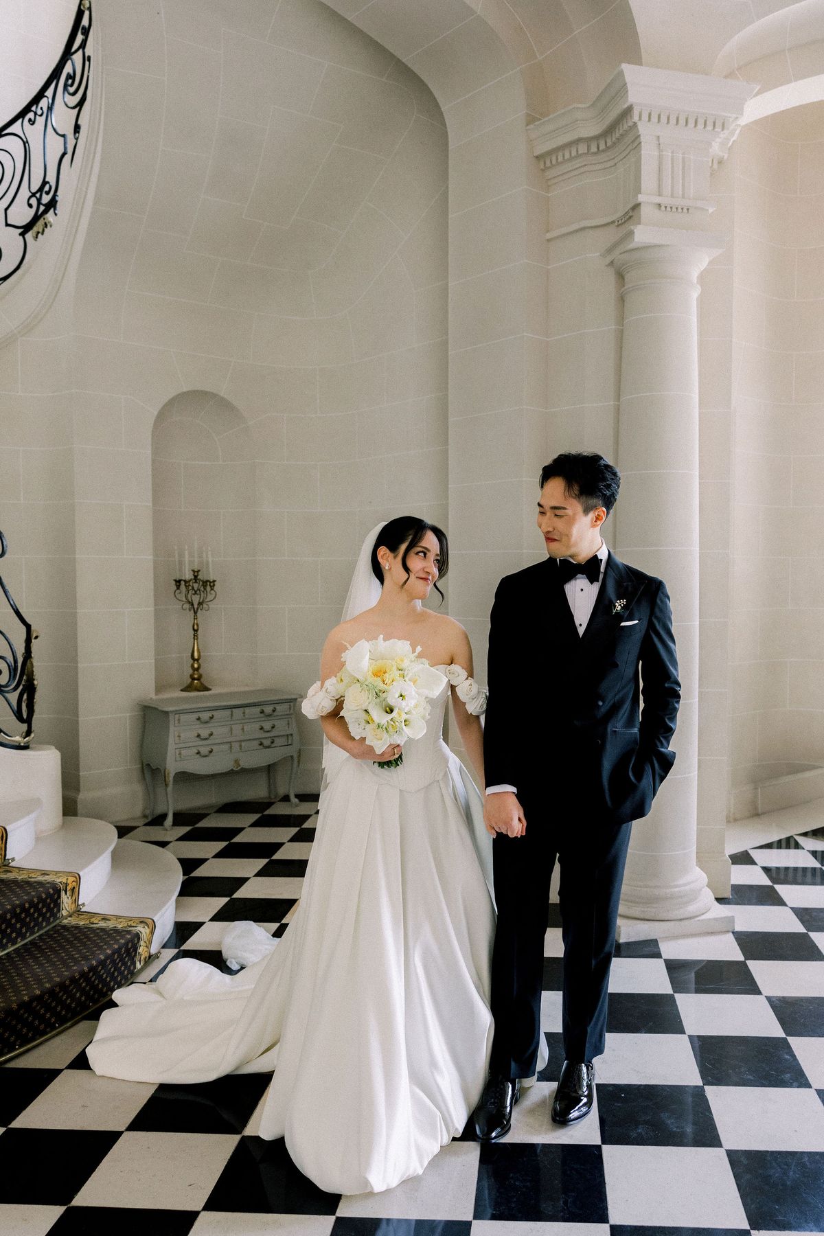The bride and groom stand together in the stone entrance hall beside a column