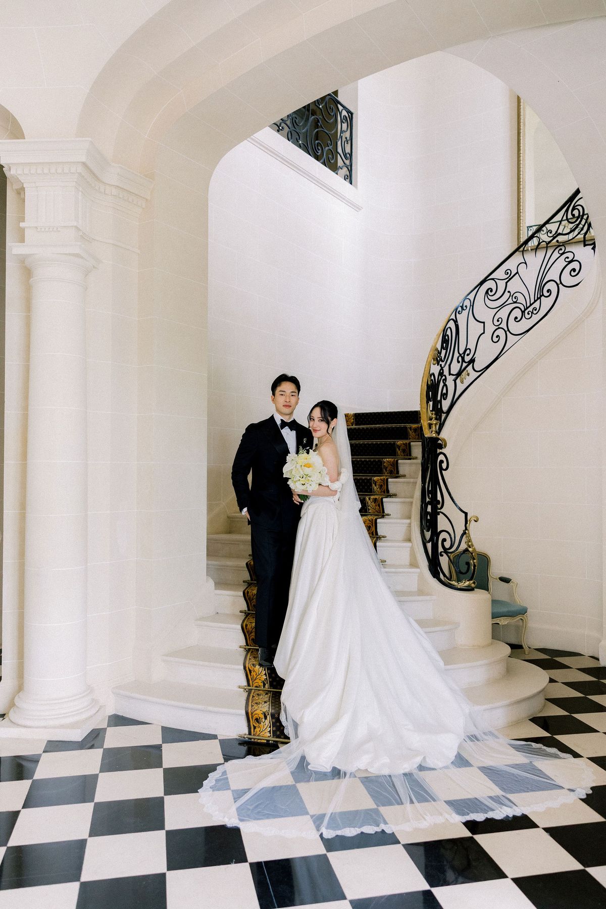 The couple stand at the foot of the curving iron-railed staircase in the chateau hall