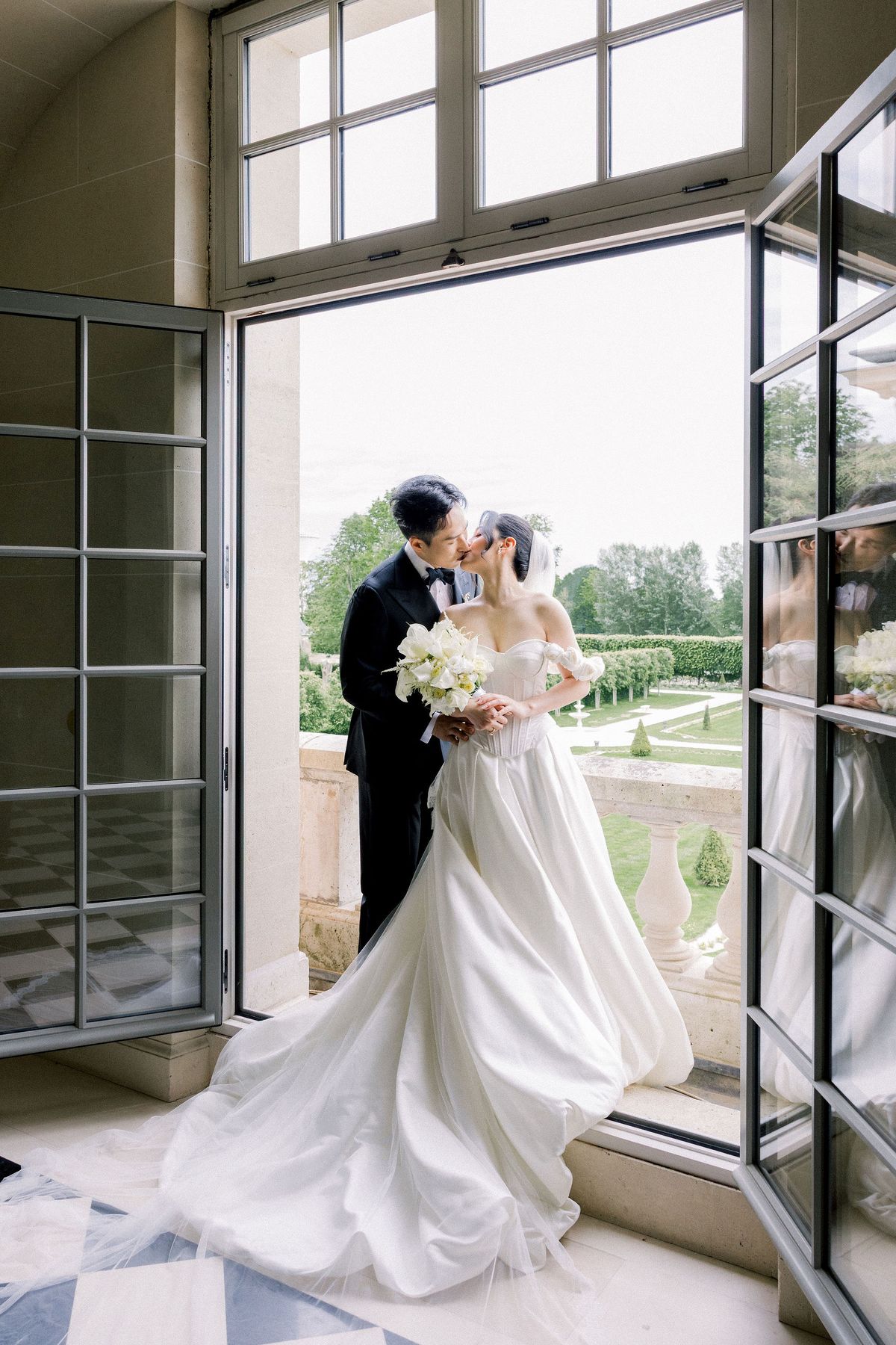 The couple kiss in an open window above the formal gardens