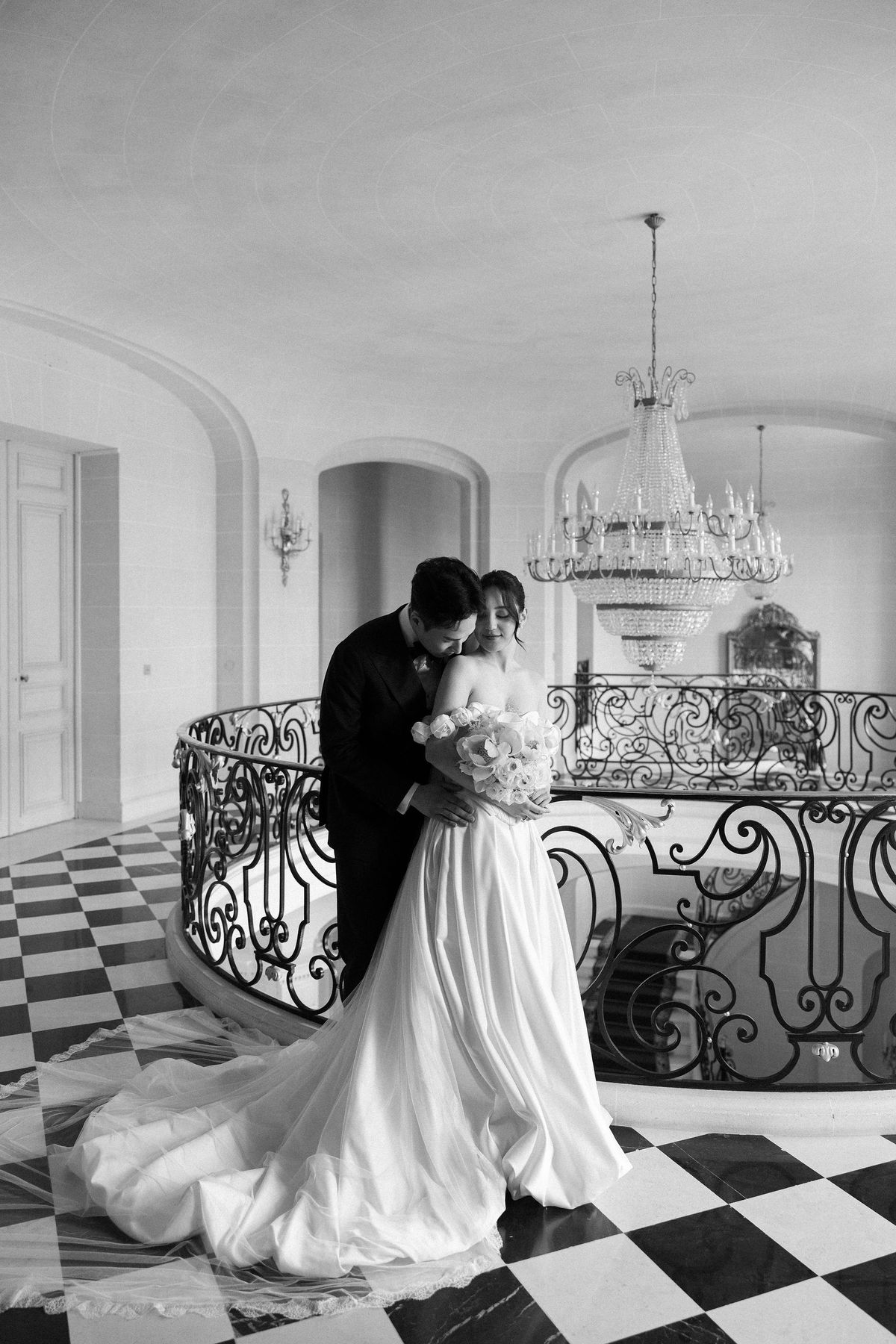 Black and white image of the couple embracing on the upper landing, the train spread across the chequerboard floor