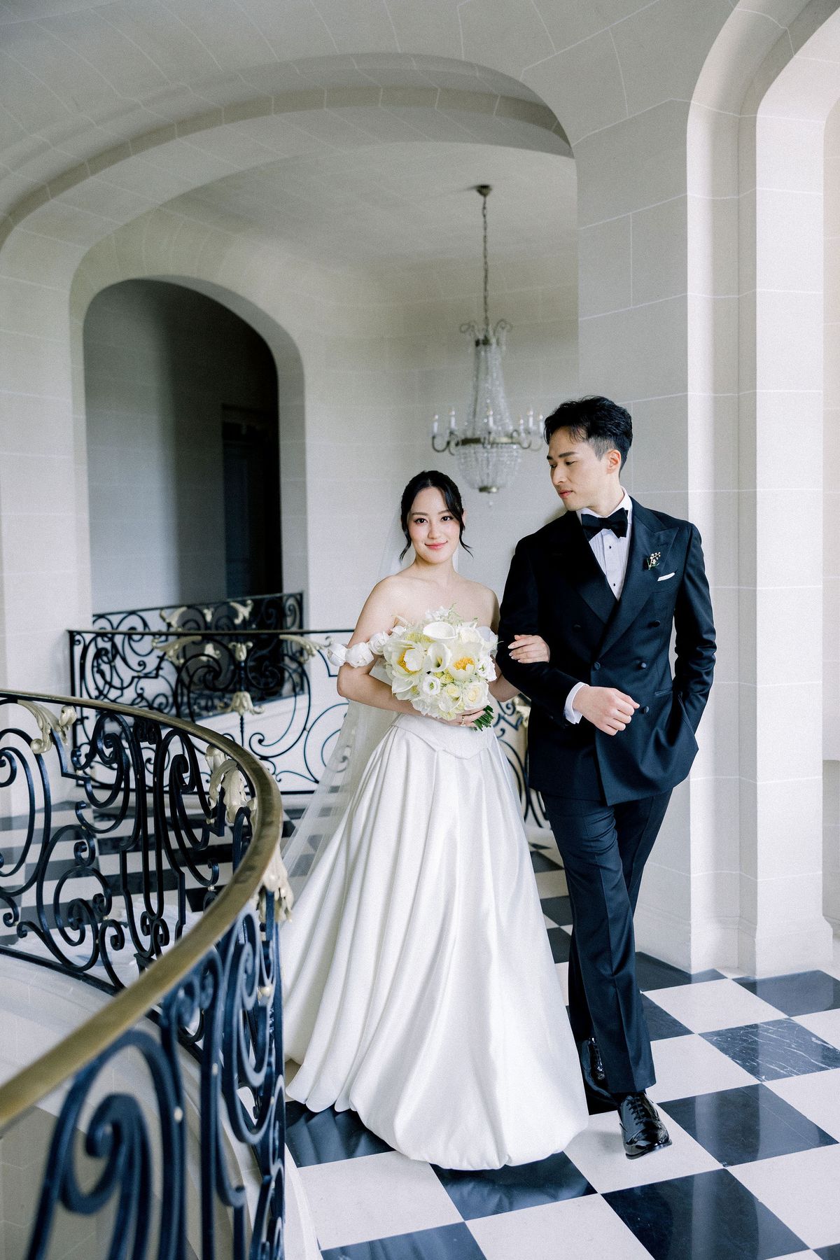 The bride takes the groom's arm on the chateau's upper landing