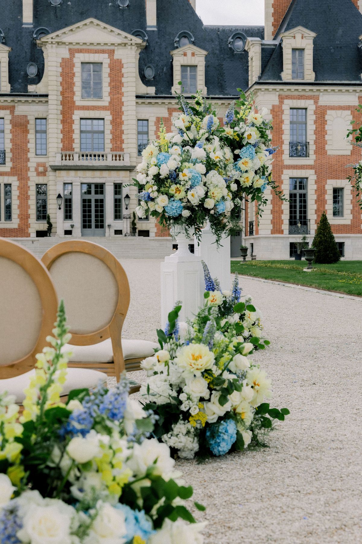 A tall arrangement of blue delphinium, white roses and yellow flowers on a plinth beside the ceremony chairs