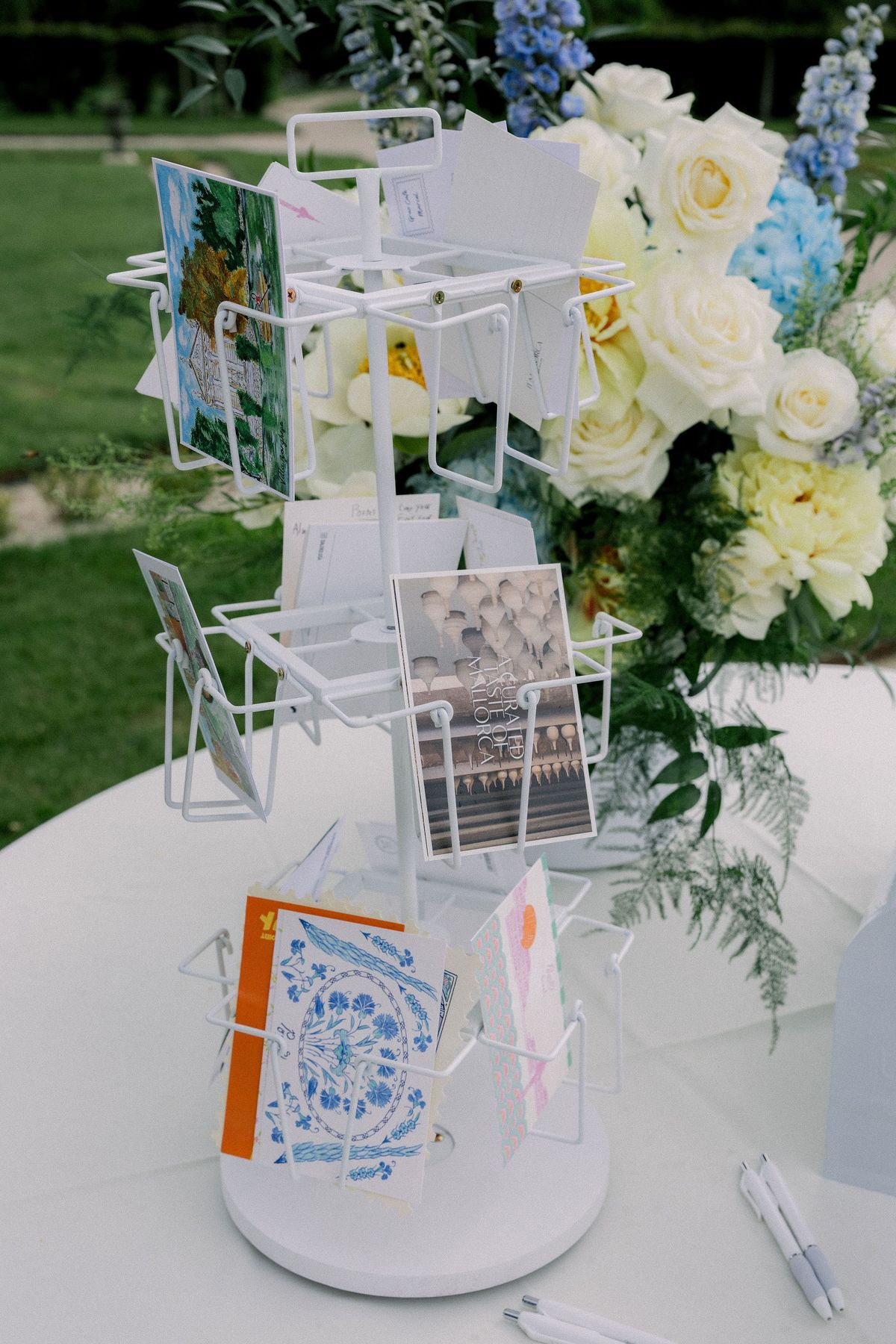A white postcard stand beside an arrangement of blue and white flowers on a table in the garden