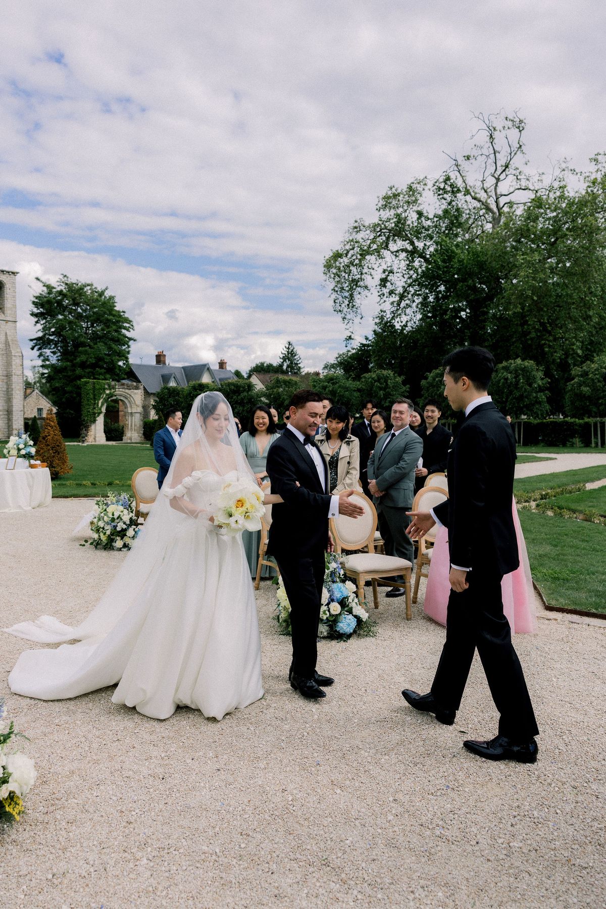 The bride in her veil is walked down the aisle as the groom steps forward to meet her