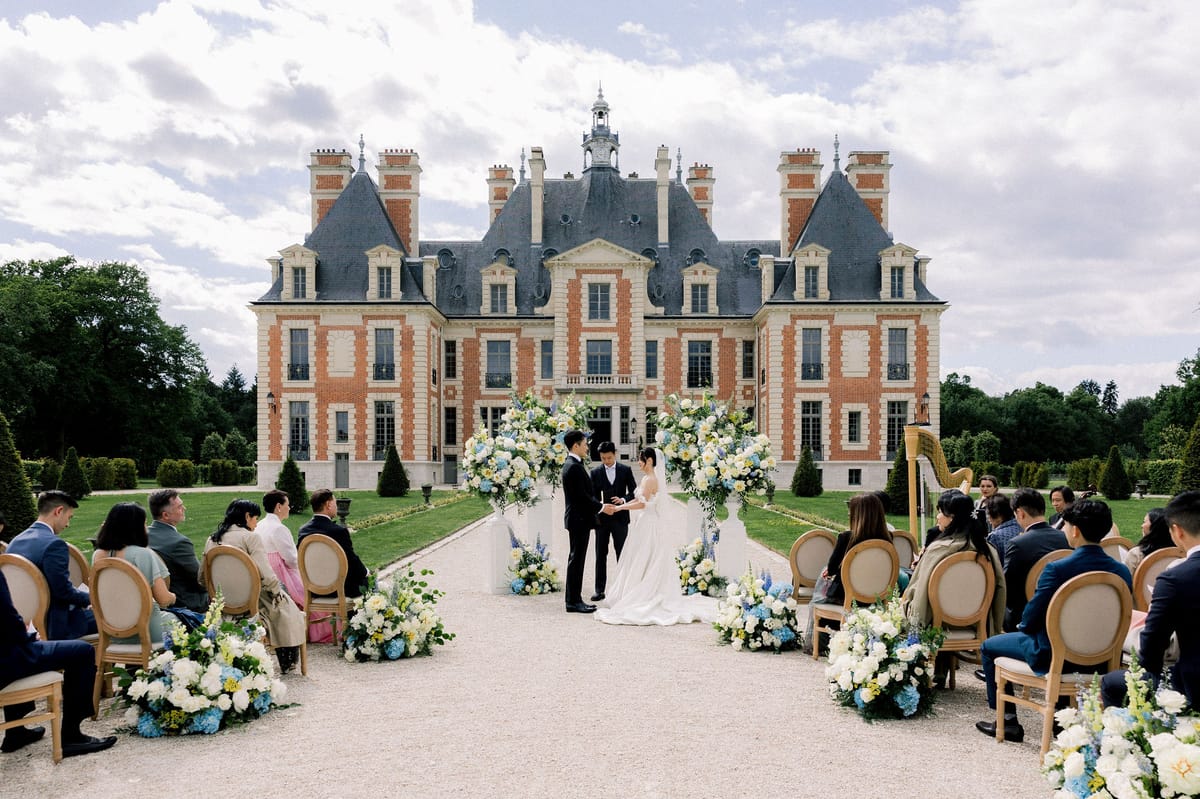 Guests seated either side of the aisle as the couple stand before the chateau facade