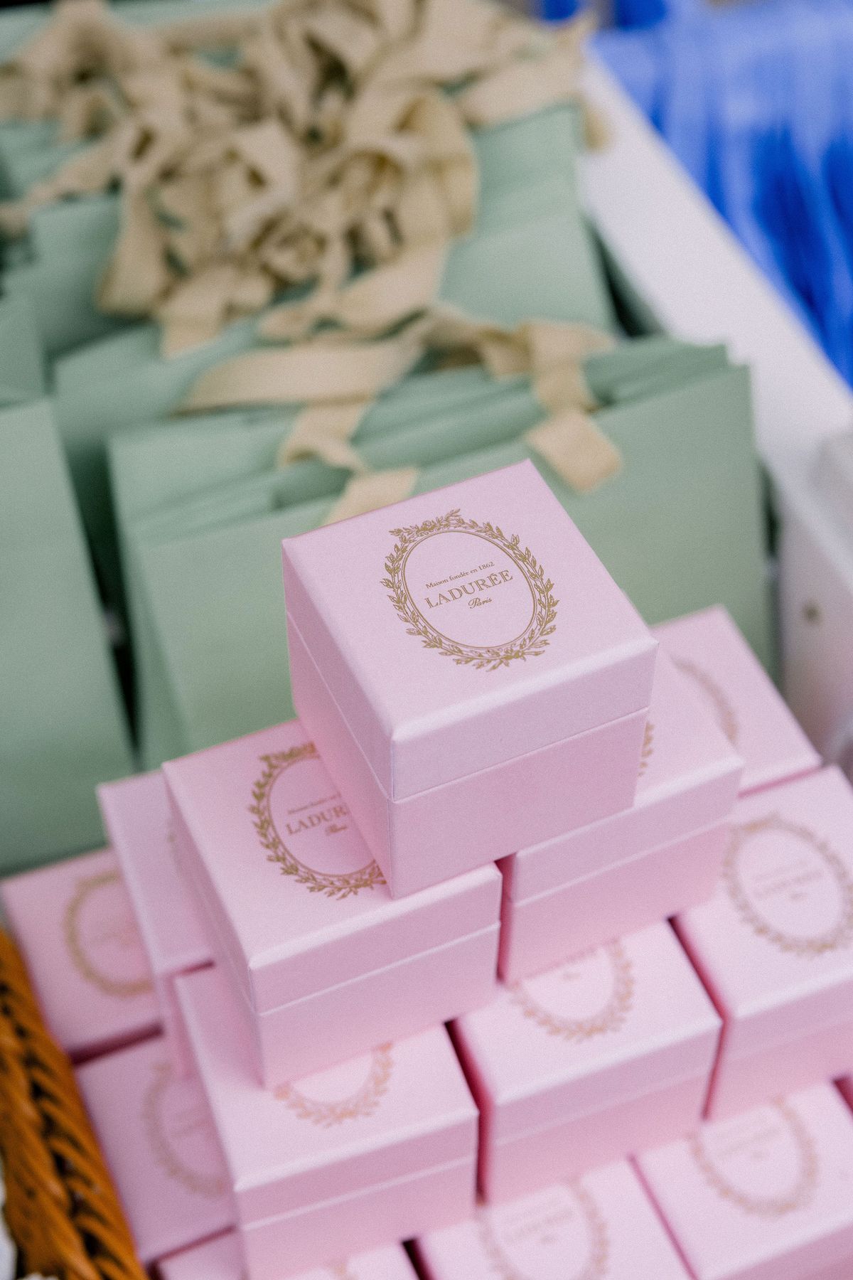 A stack of pink Ladurée boxes with green gift bags behind