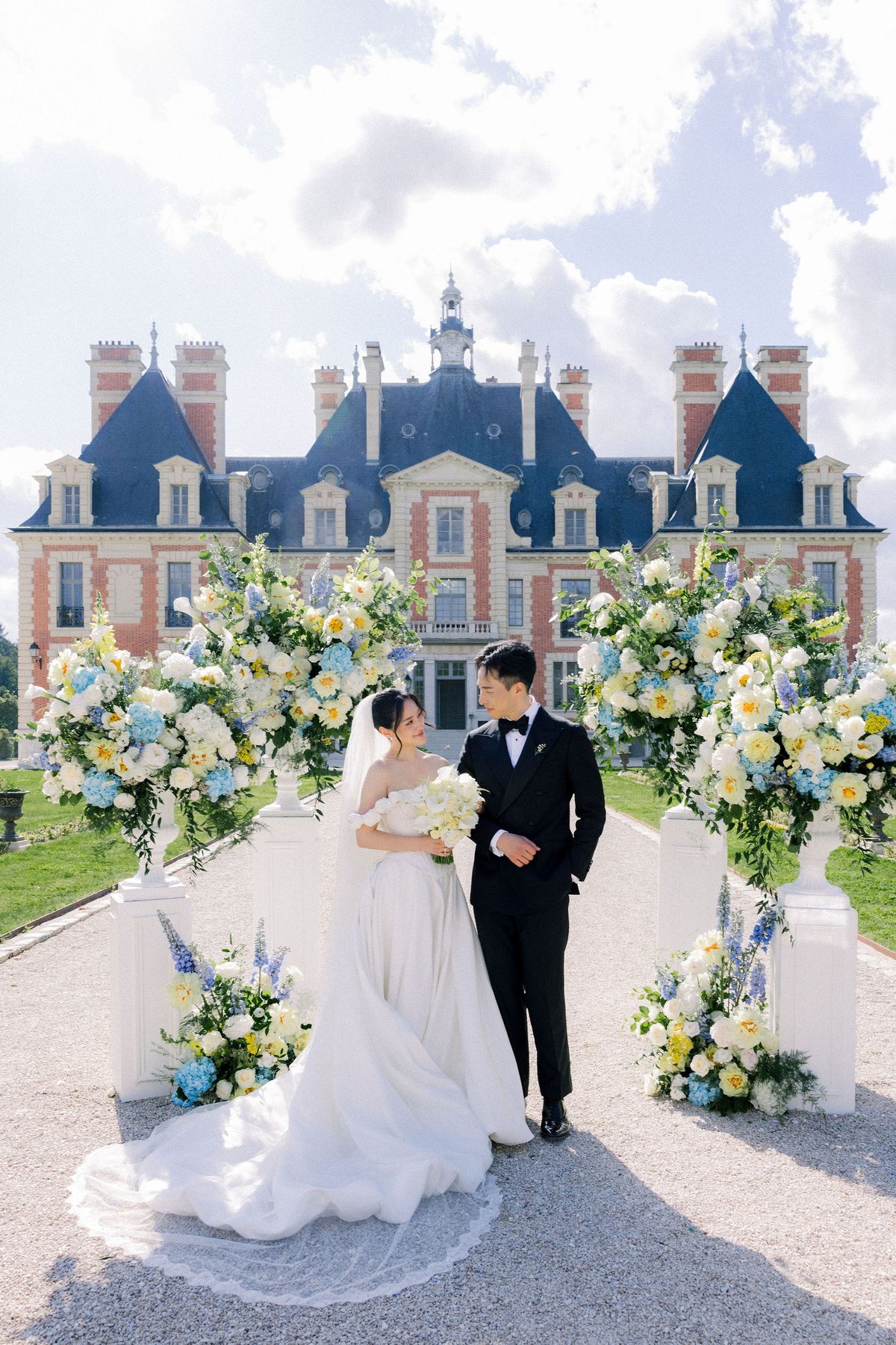 The bride looks up at the groom between the ceremony flowers in front of the chateau