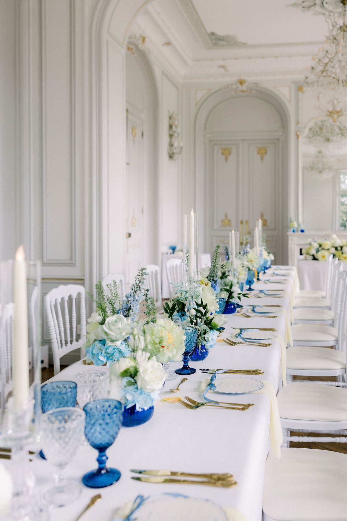 White chairs line a long table set with blue goblets and candles in the chateau salon