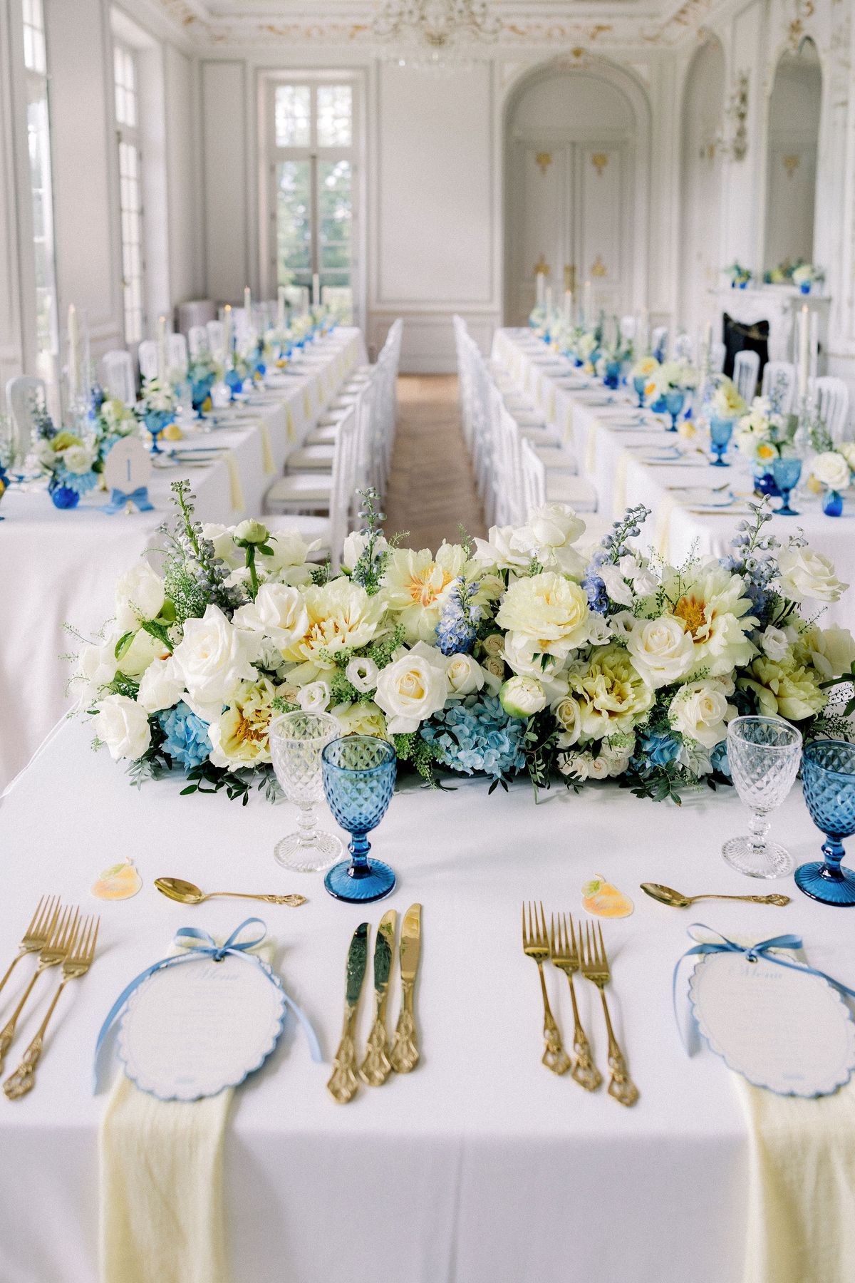 Two long tables of white and blue flowers and gold cutlery run the length of the salon
