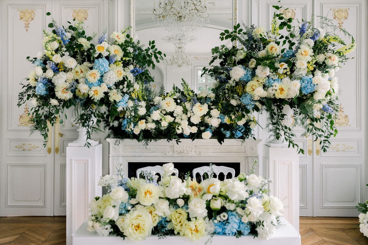 The couple's table in front of a white marble fireplace banked with blue and white flowers