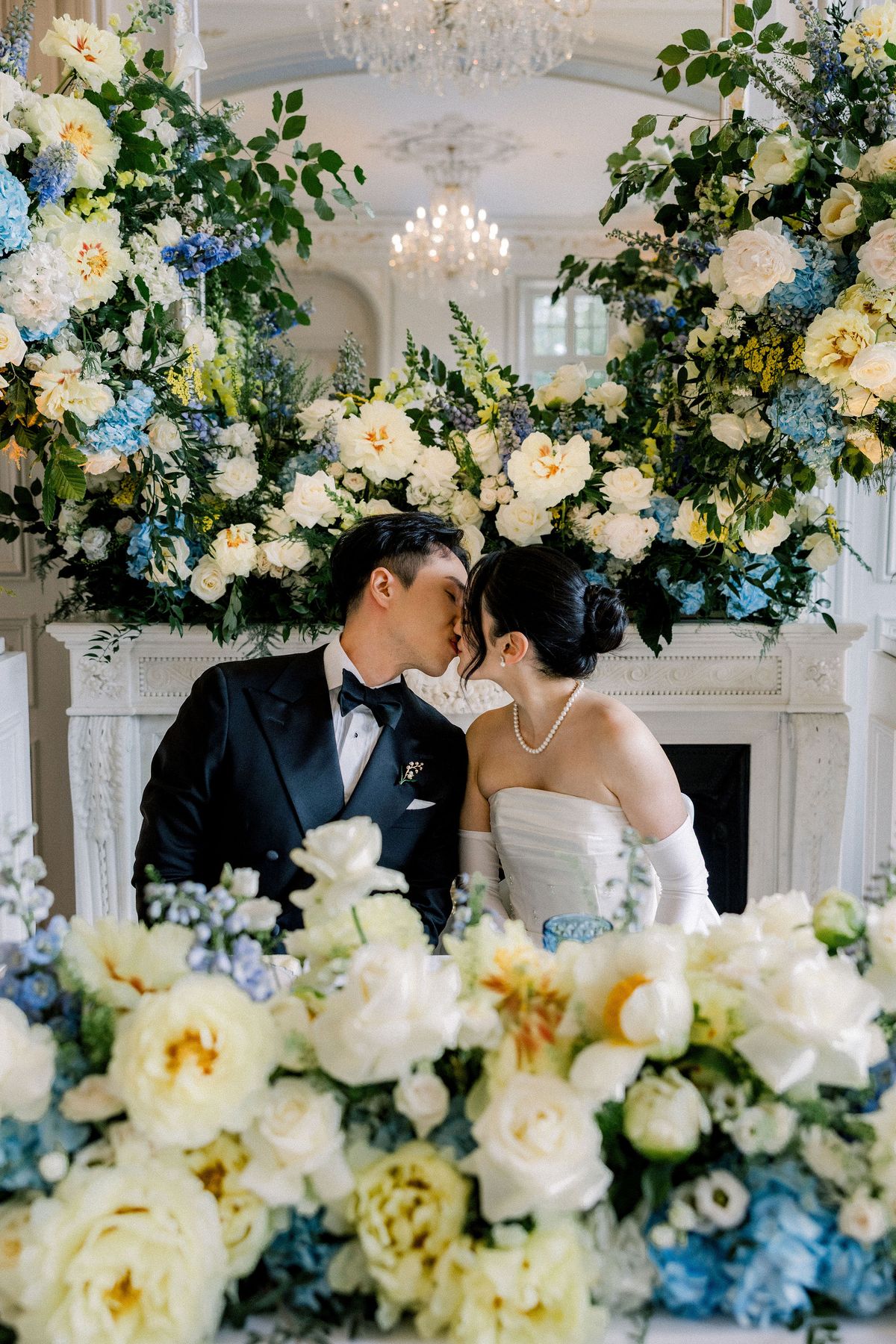 The couple kiss at their table beneath the fireplace flowers