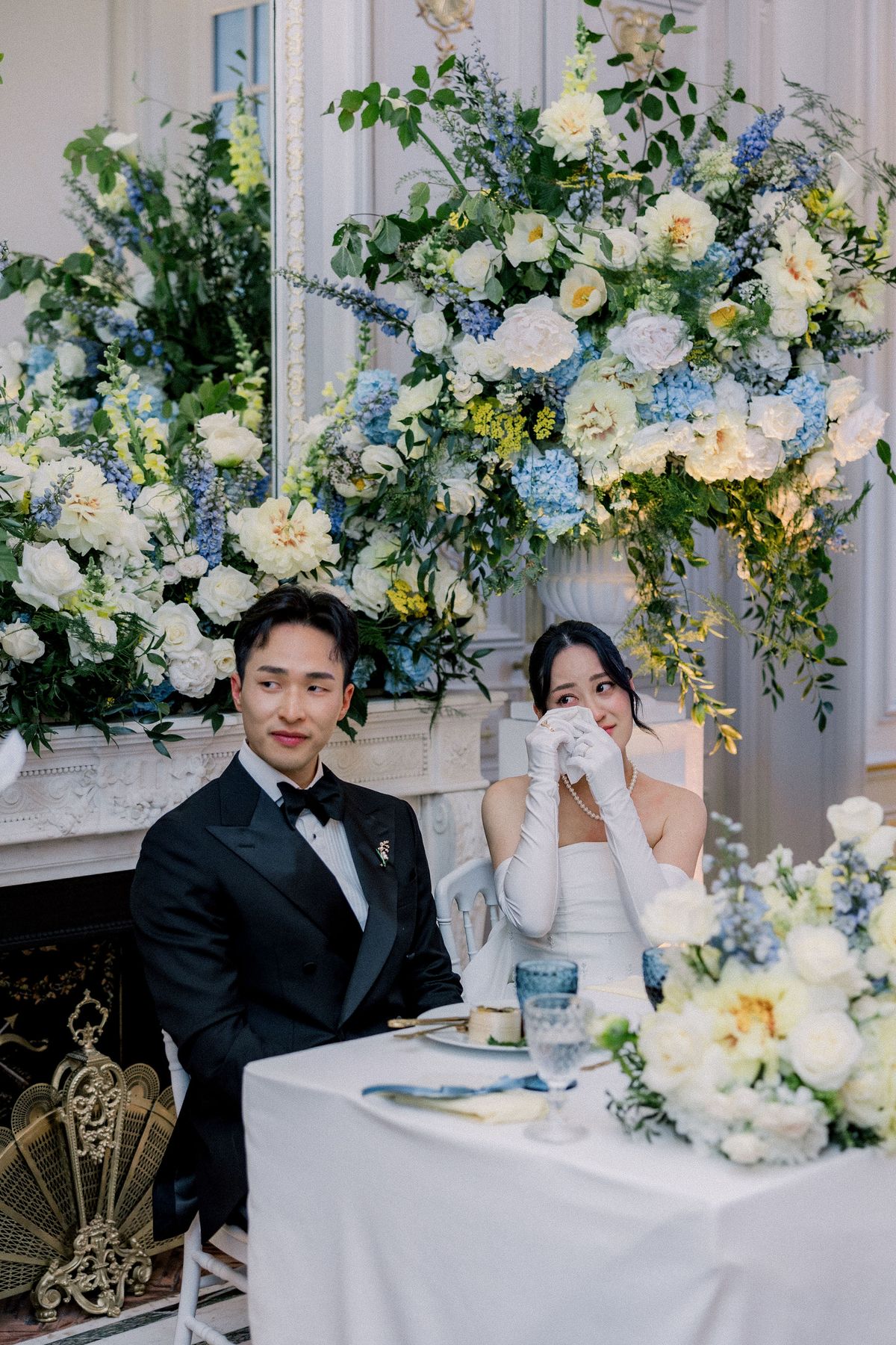 The groom smiles as the bride holds a tissue to her face at their table