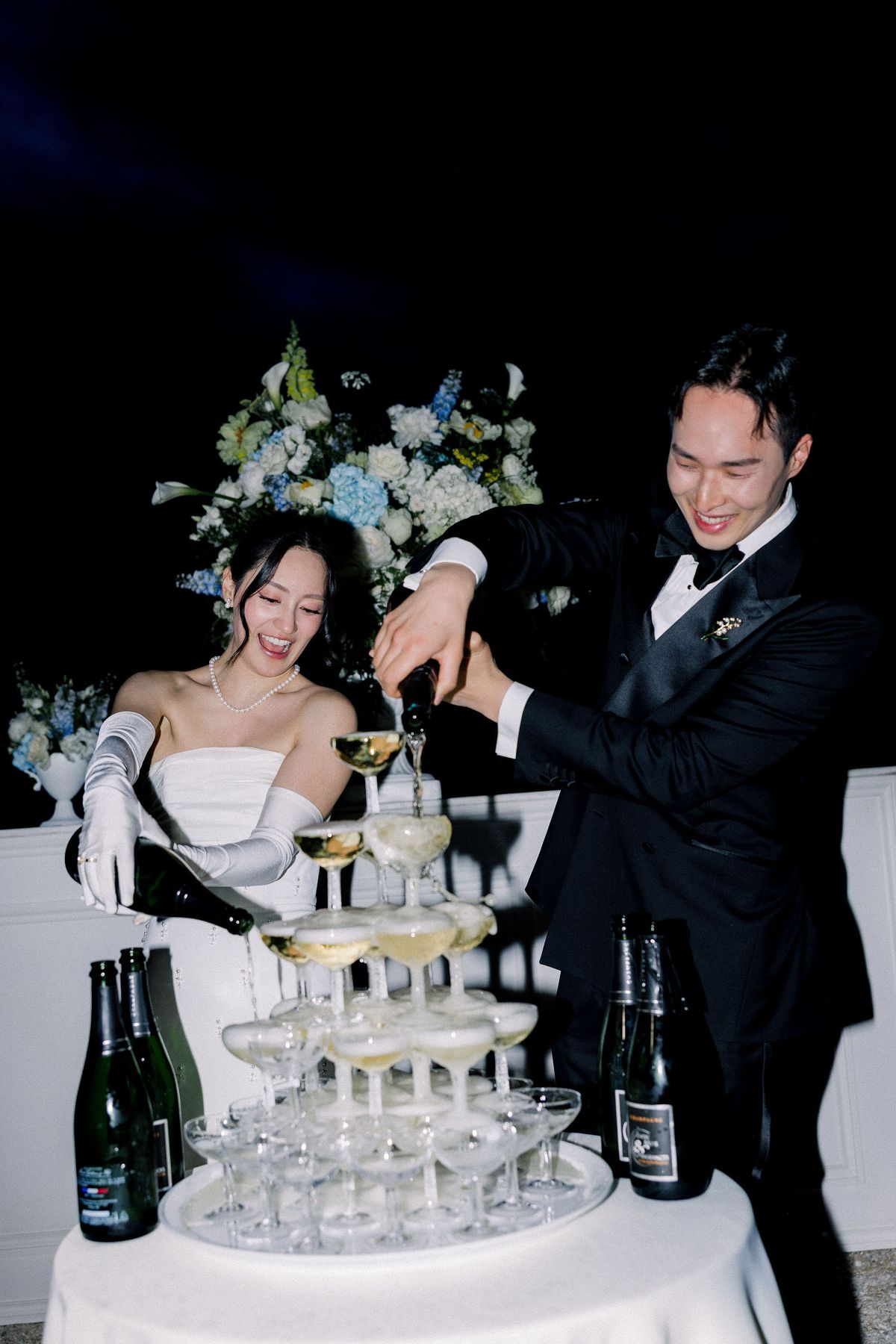 The couple pour champagne into a coupe tower at night