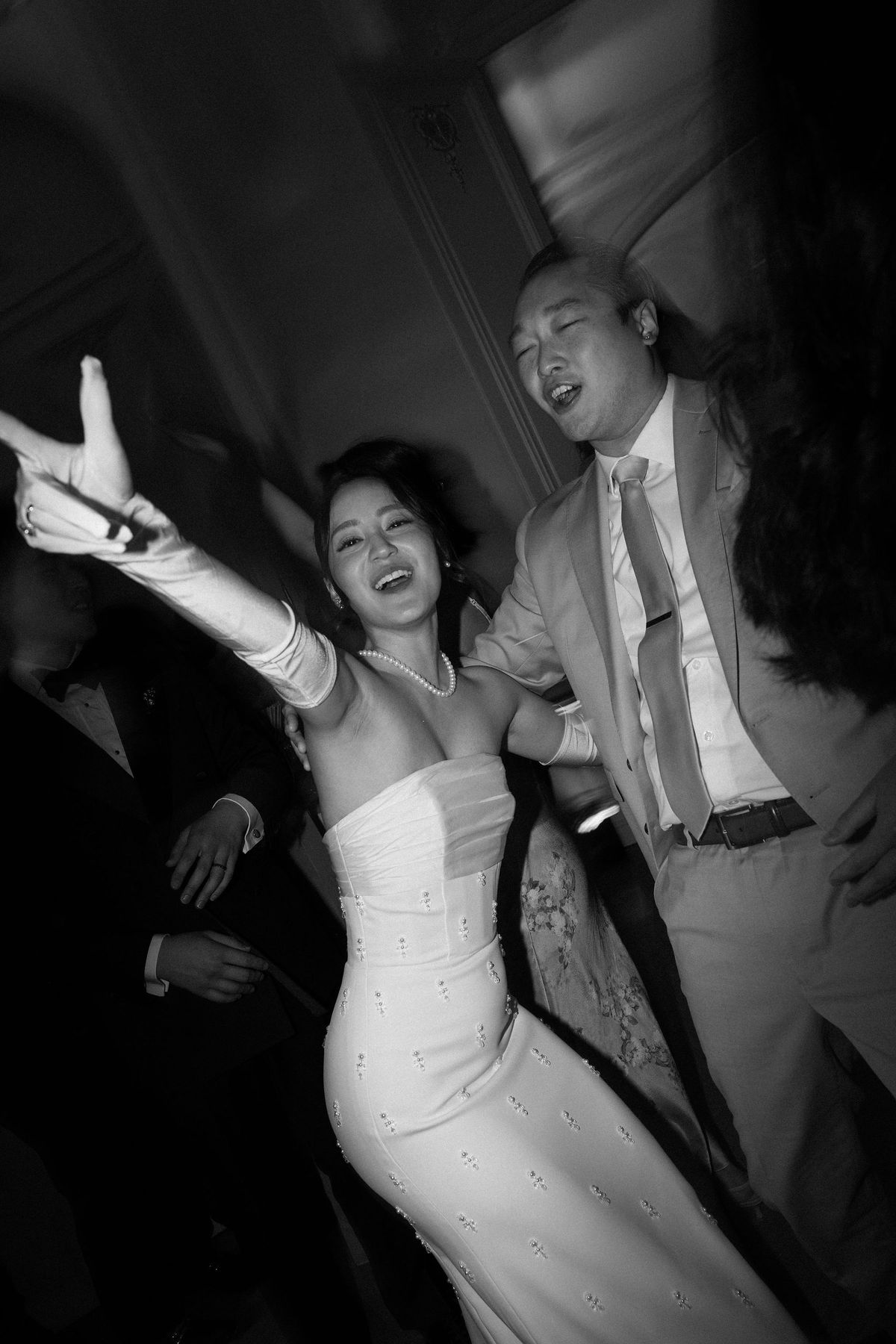 Black and white image of the bride and a guest dancing with arms raised