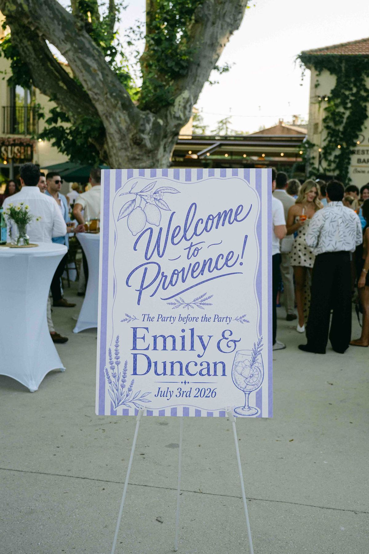 A blue and white easel sign reading 'Welcome to Provence!' stands outside under a large tree while guests gather behind.