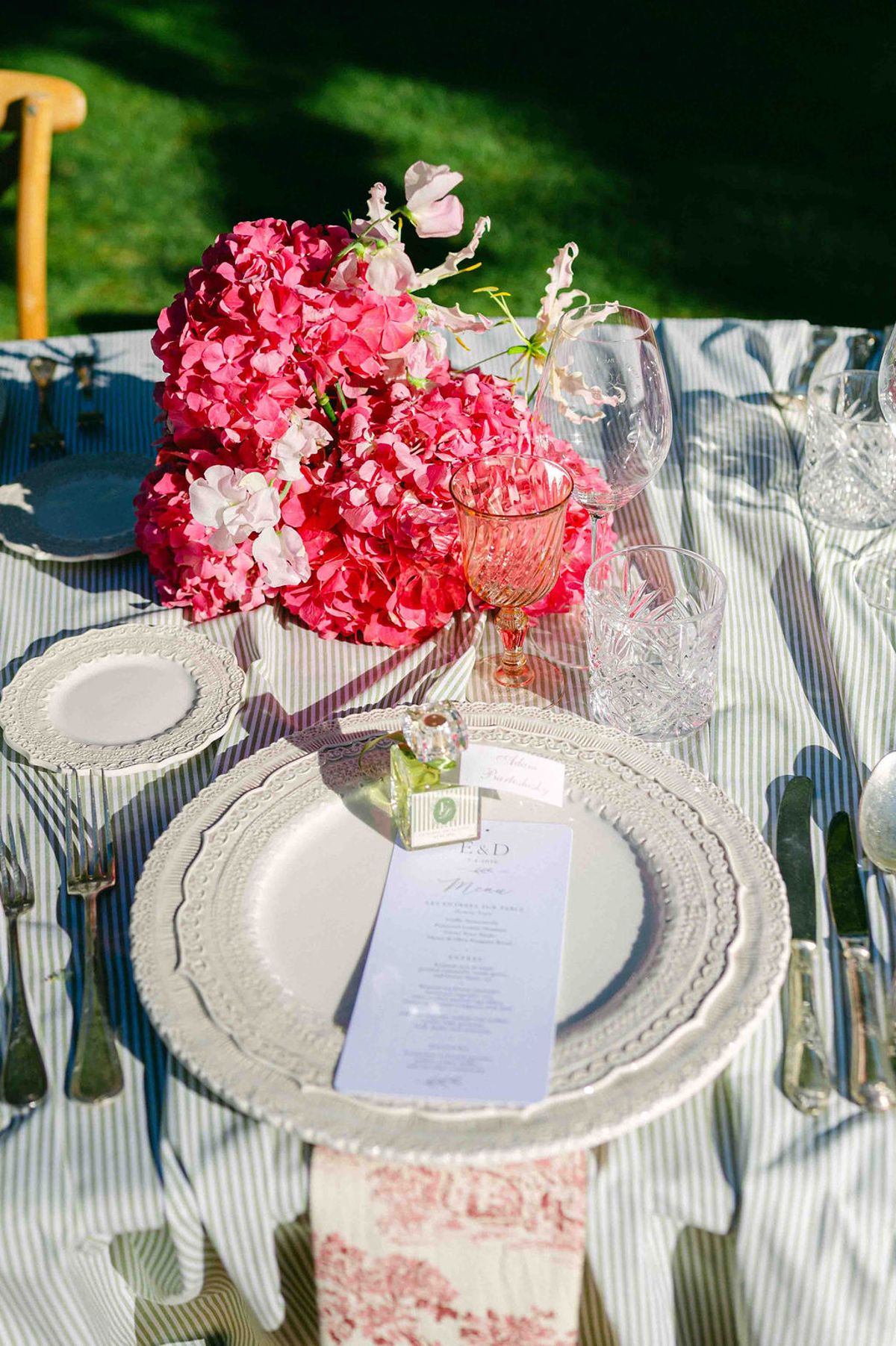 A striped tablecloth holds a plate with a menu card, glasses and a centrepiece of bright pink hydrangeas.
