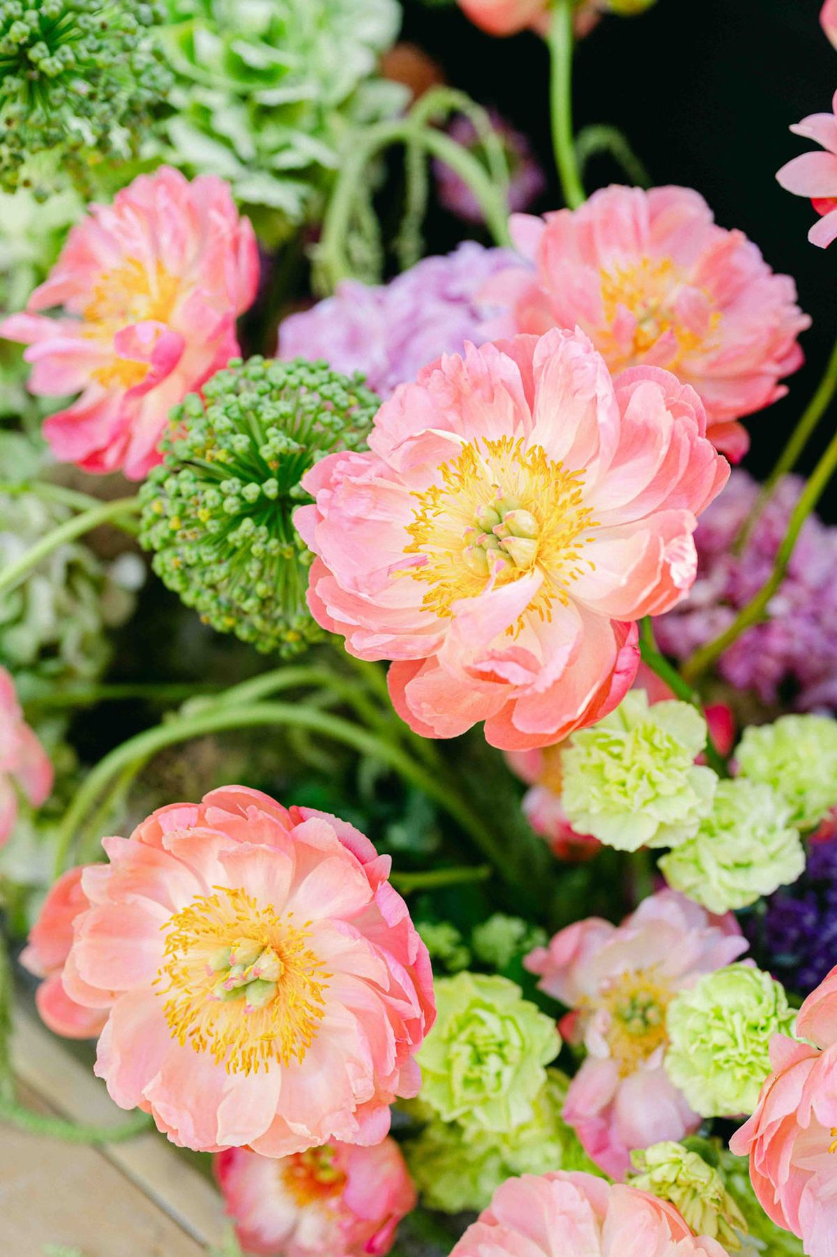 Close-up of coral pink peonies with purple blooms and lime green flowers in a colourful arrangement.