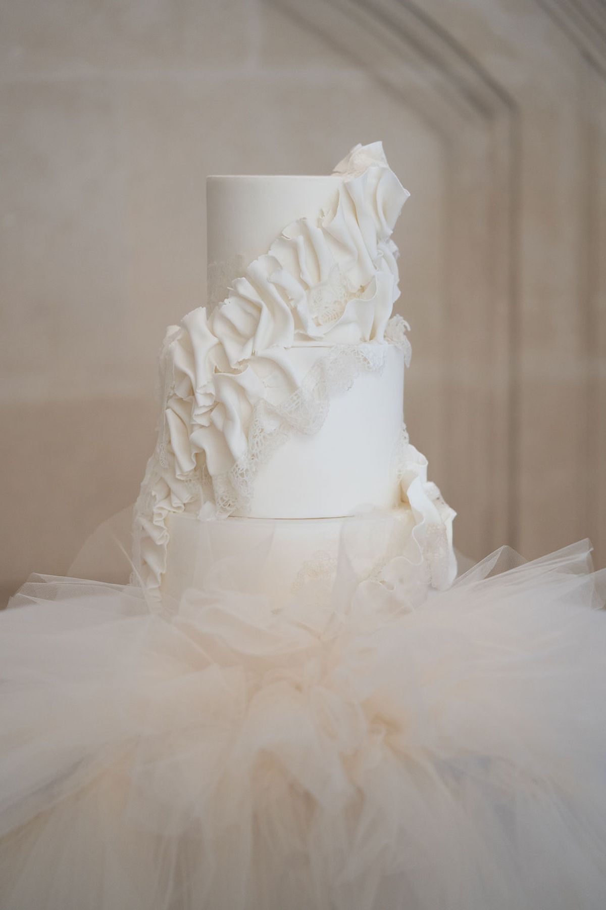 Ruffled tiered cake set on tulle against a stone wall