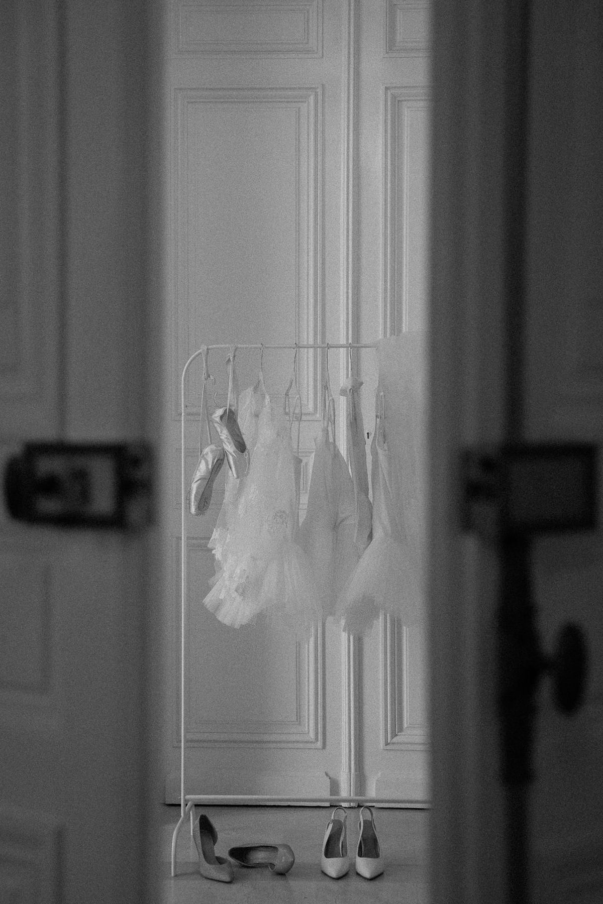 Black and white frame of tutus hung on a rail with shoes lined beneath