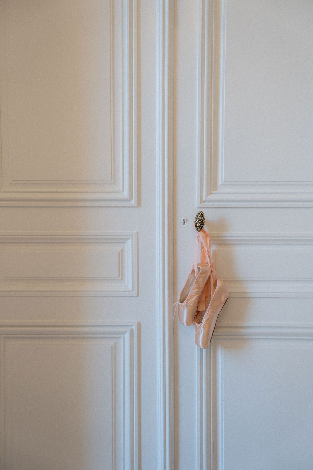 Pair of satin pointe shoes hung from the handle of a panelled door
