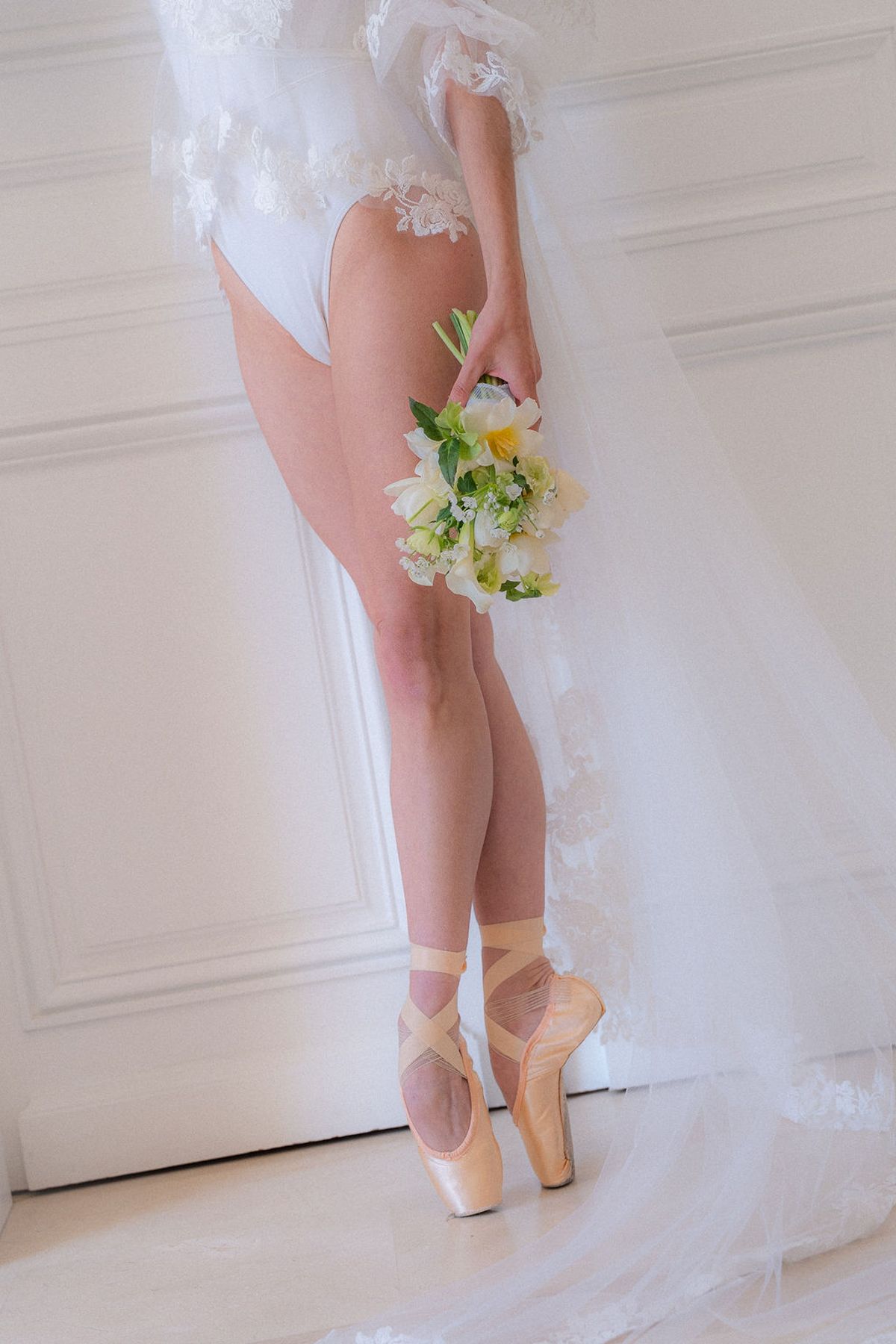 Detail of legs en pointe in satin shoes beside a bouquet and tulle