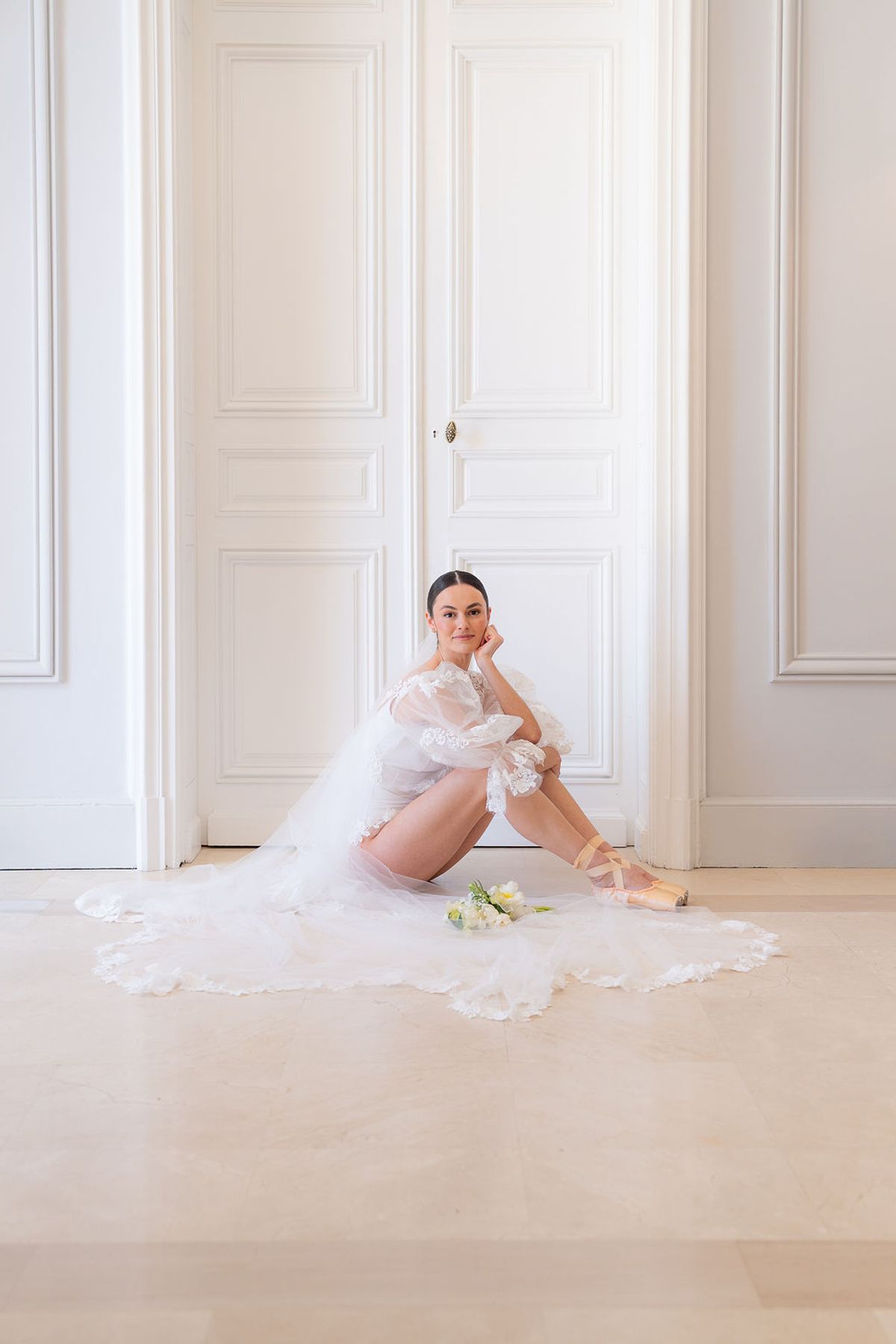 Dancer seated on the floor of a white room, tulle pooling around her