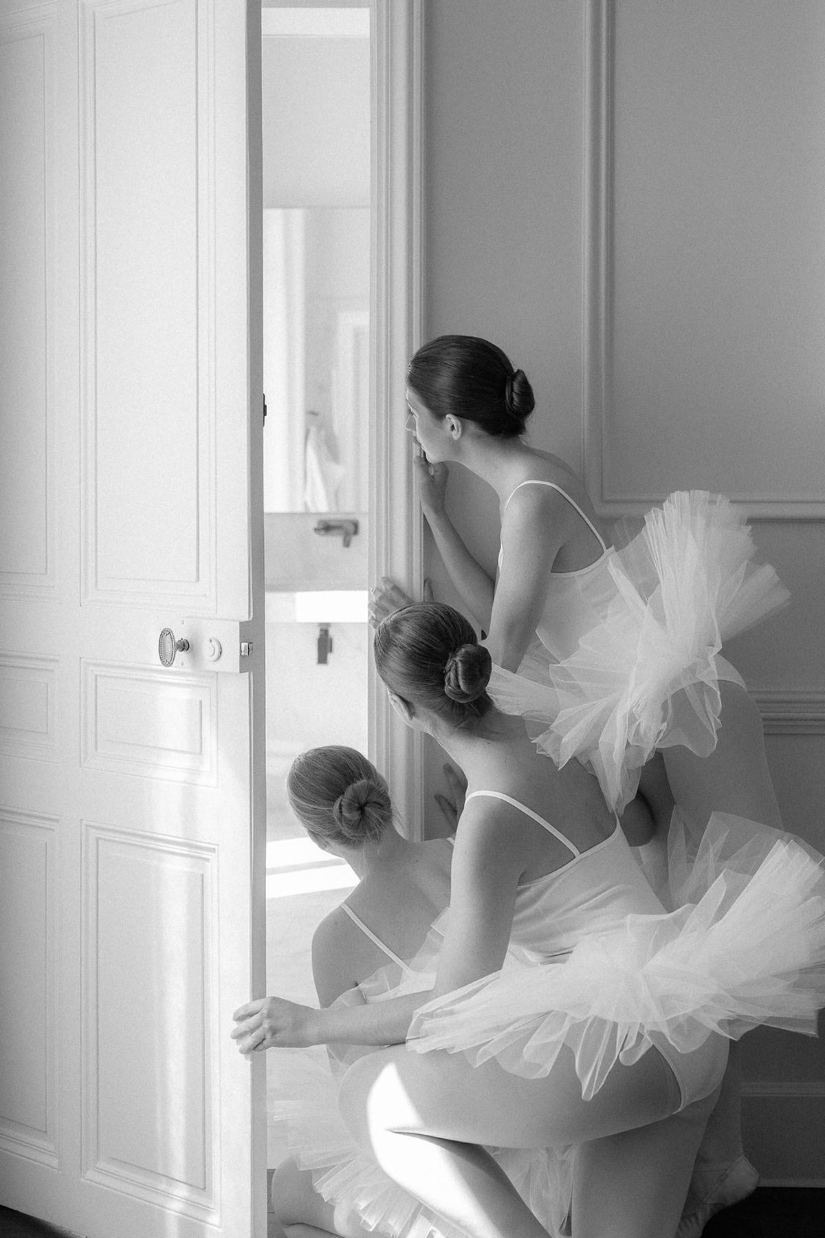 Black and white frame of dancers in tutus layered in a panelled doorway