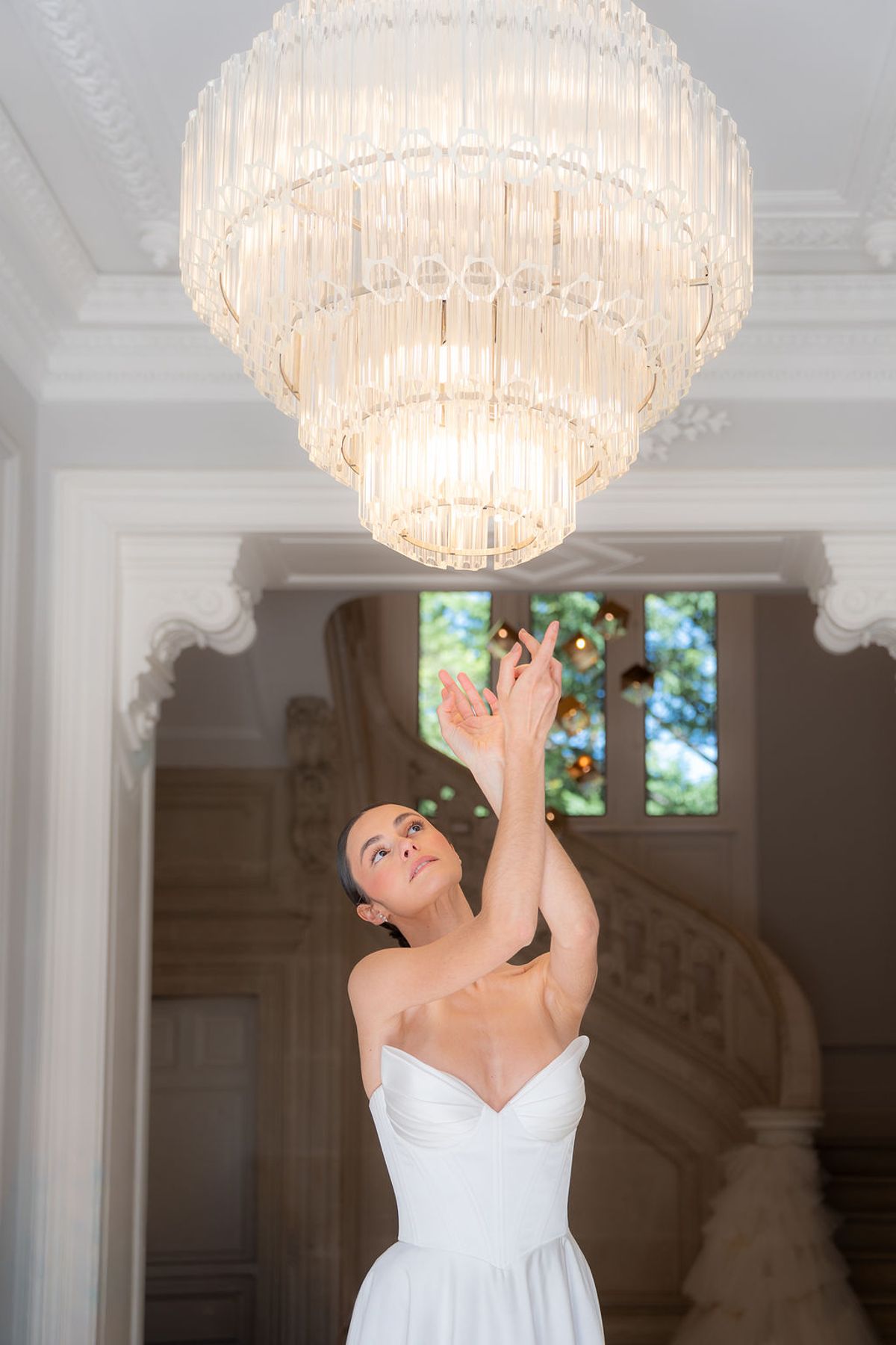 Dancer reaching upward beneath a tiered crystal chandelier on a stone staircase