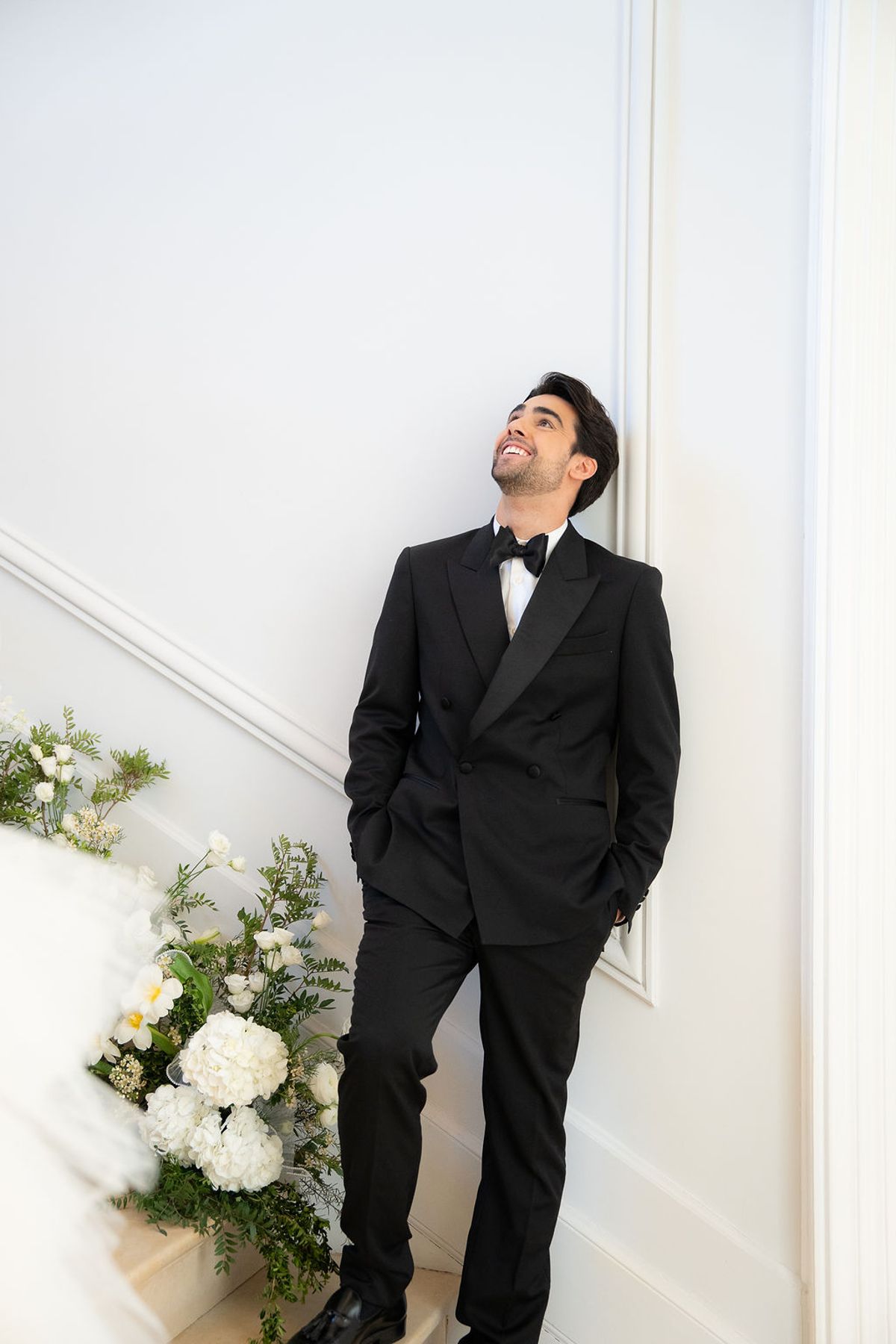Dancer in black tie leaning against a panelled doorway beside a white floral arrangement