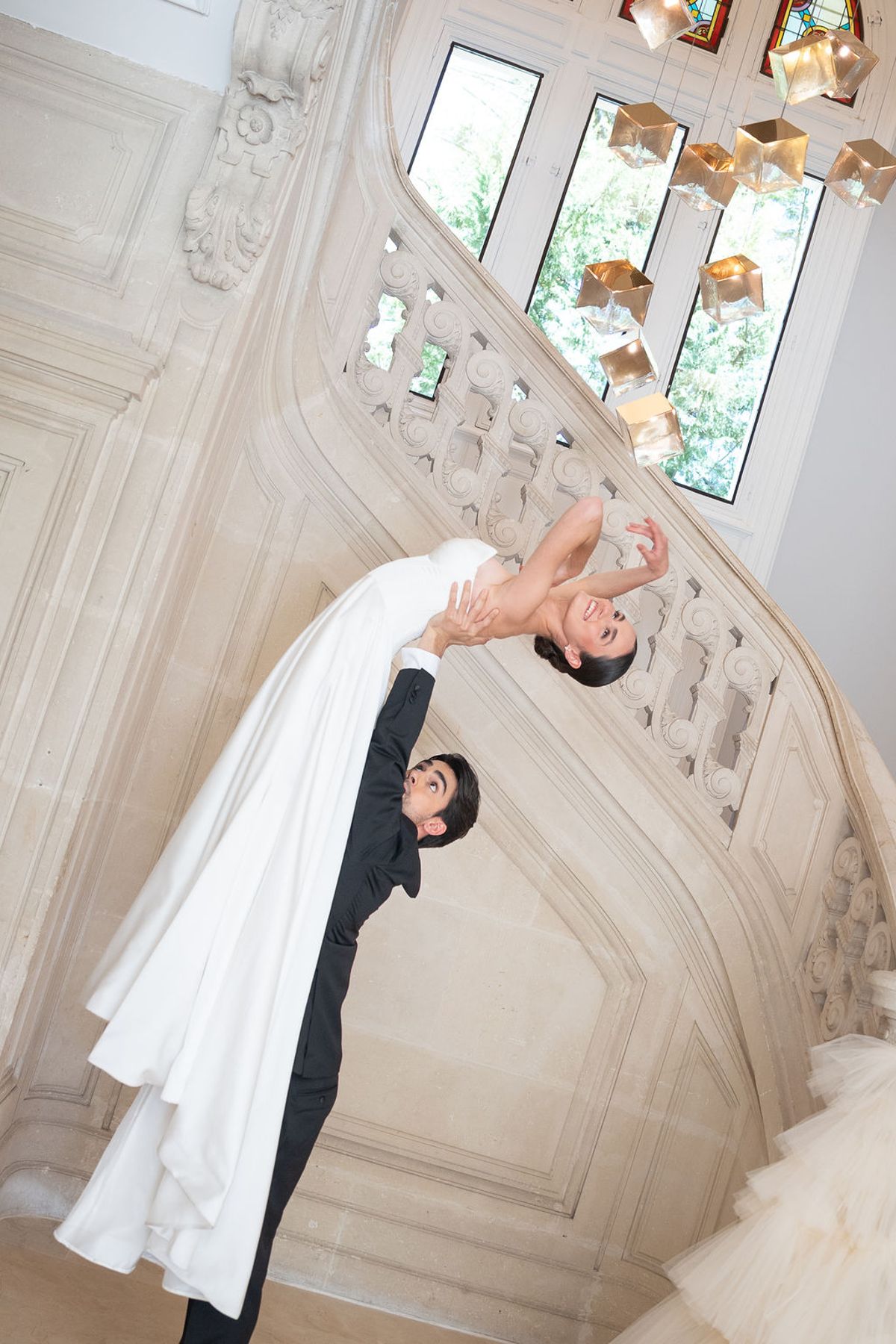 Two dancers posed against a moulded wall, gown fabric spread across the floor