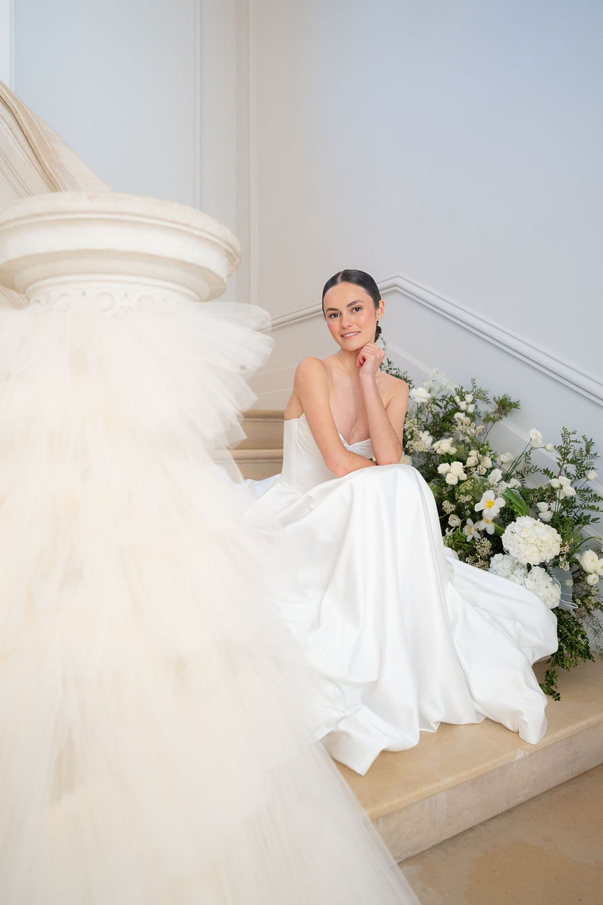 Dancer seated on stone steps in a layered tulle gown beside white florals