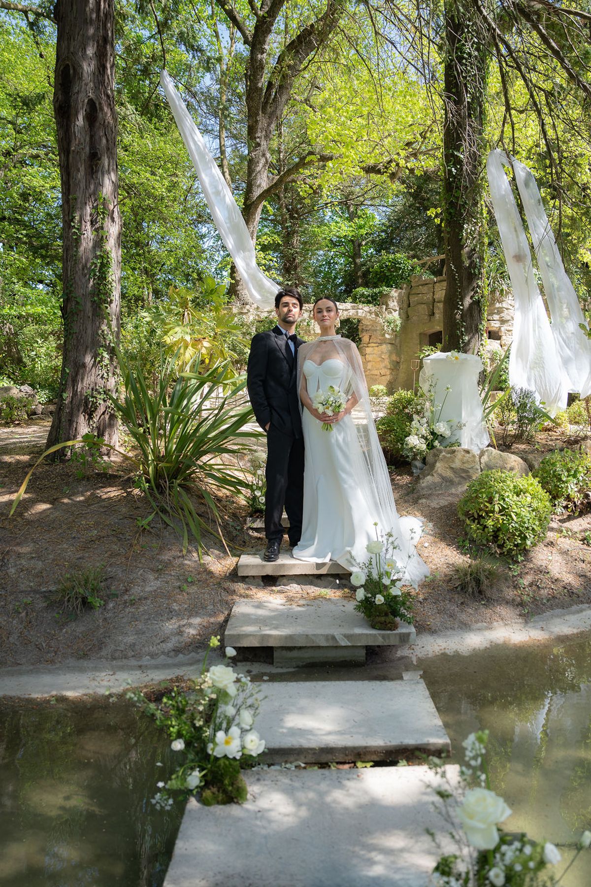 Two dancers standing on stone steps over water beneath hanging fabric panels