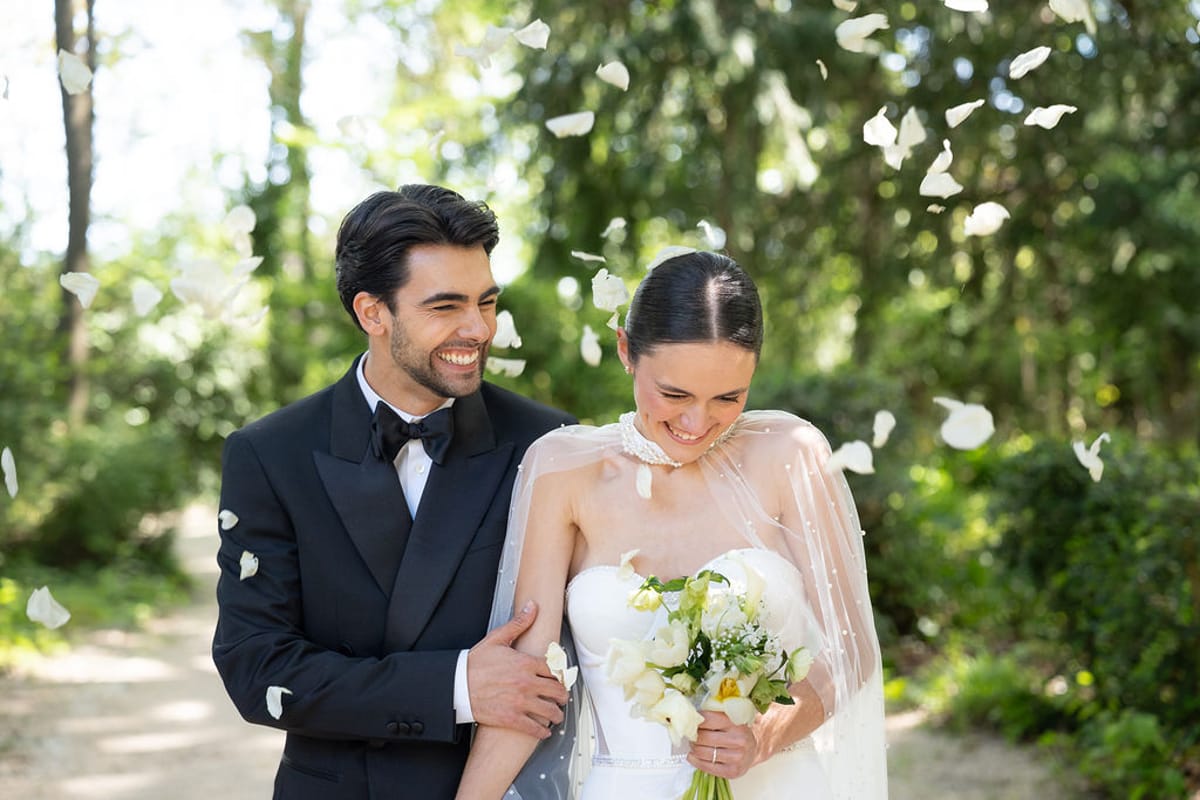 Two dancers walking together beneath falling petals on a tree-lined path