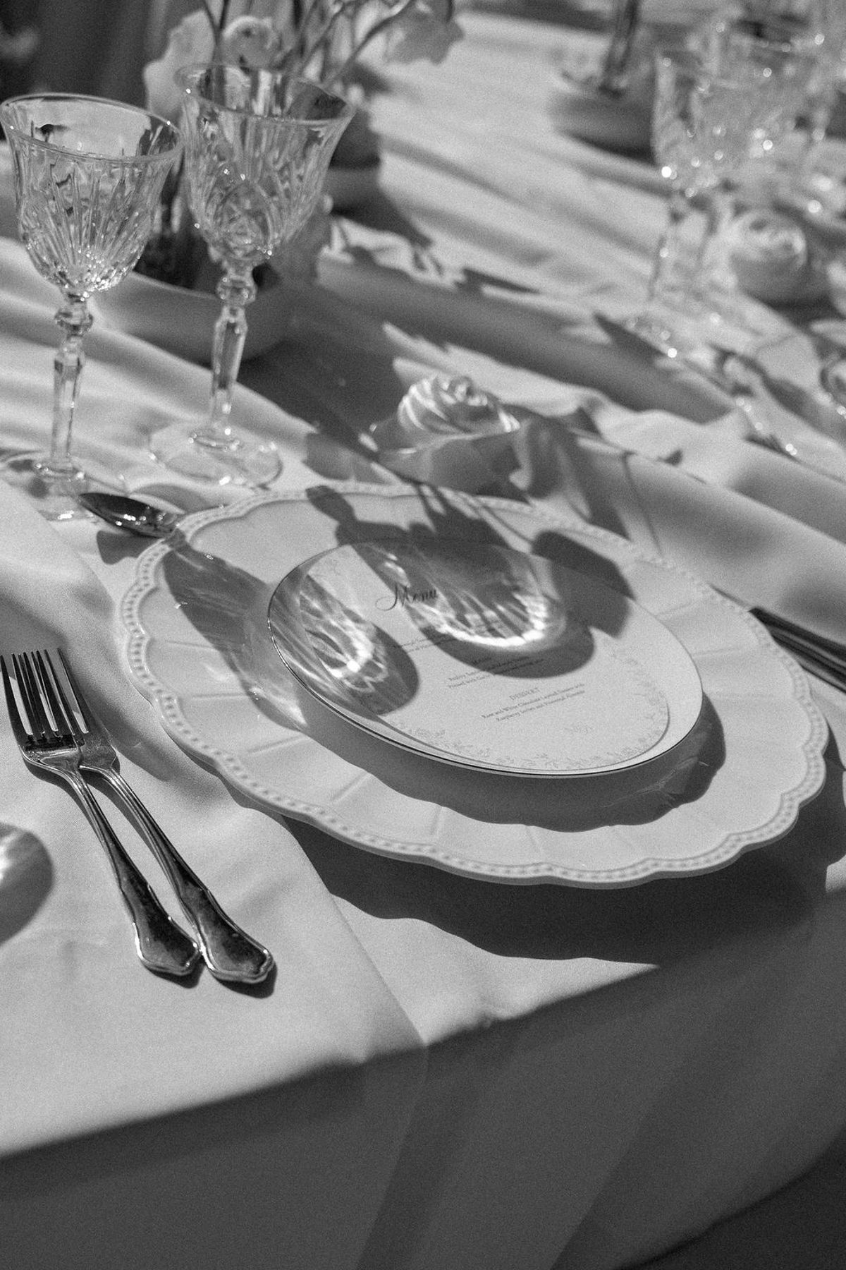 Black and white detail of silver cutlery, crystal and a scalloped charger