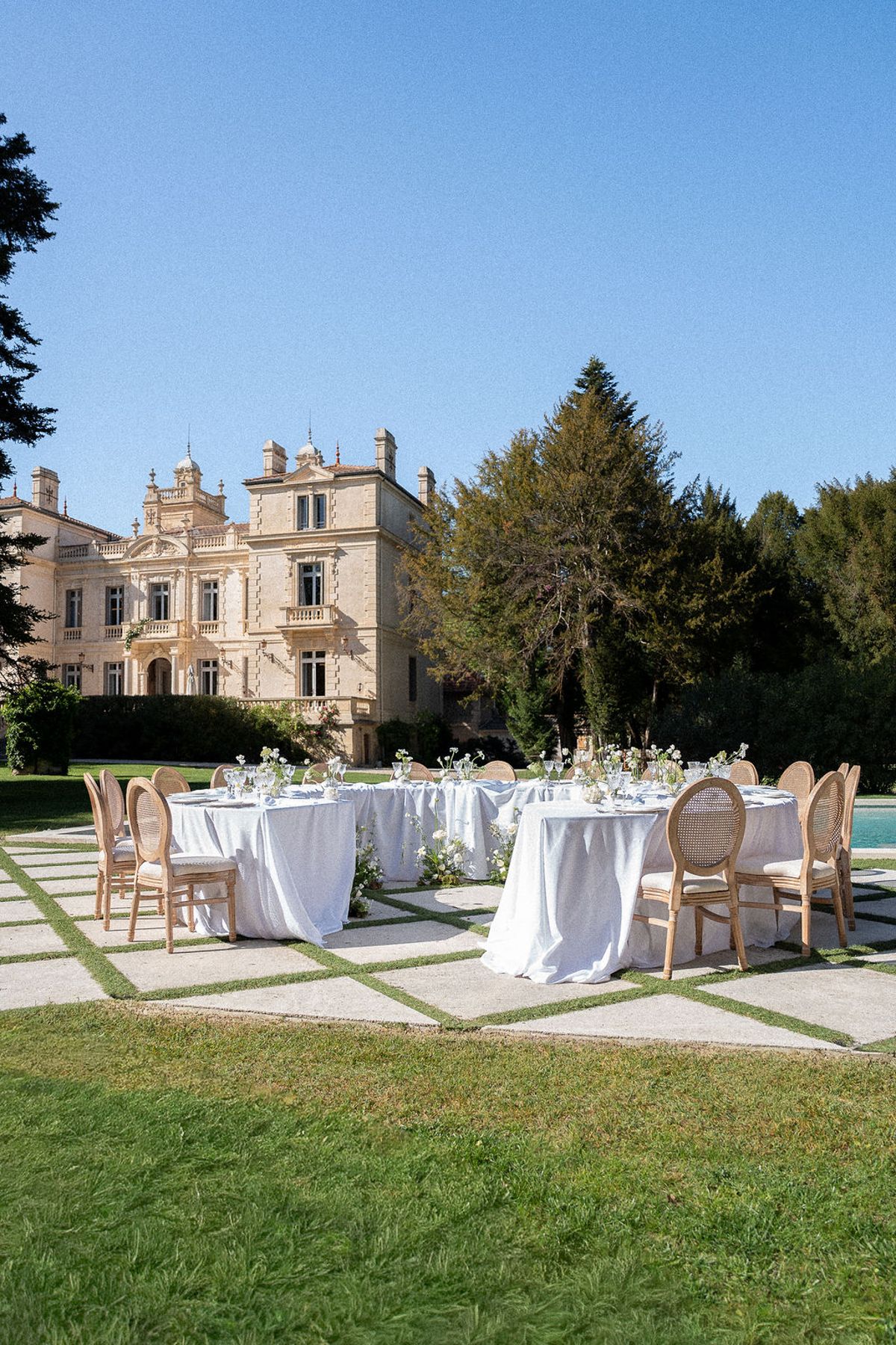 Round tables set on the lawn in front of Château des Trois Fontaines under a clear sky