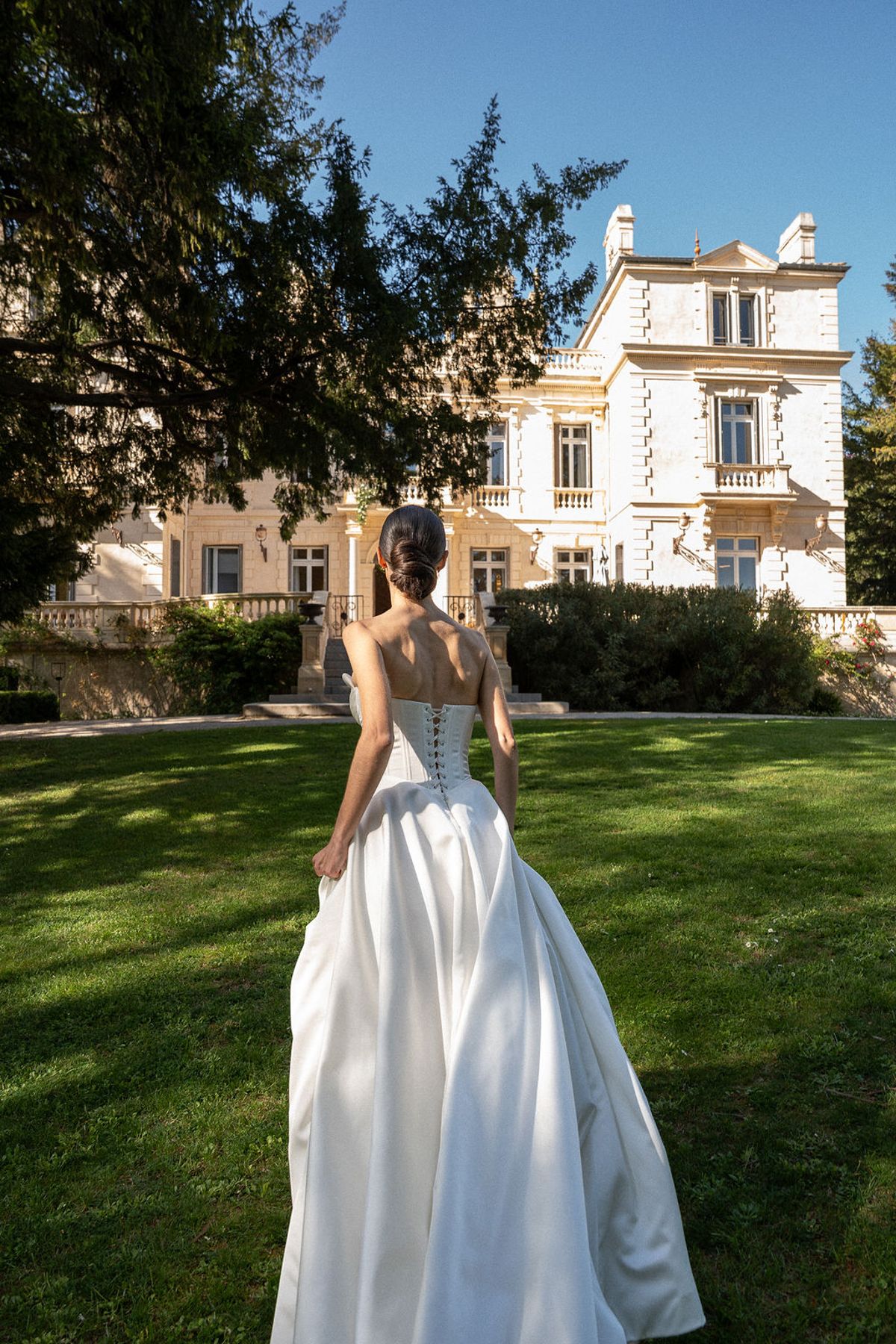 Dancer walking away across the lawn toward Château des Trois Fontaines in a full satin skirt