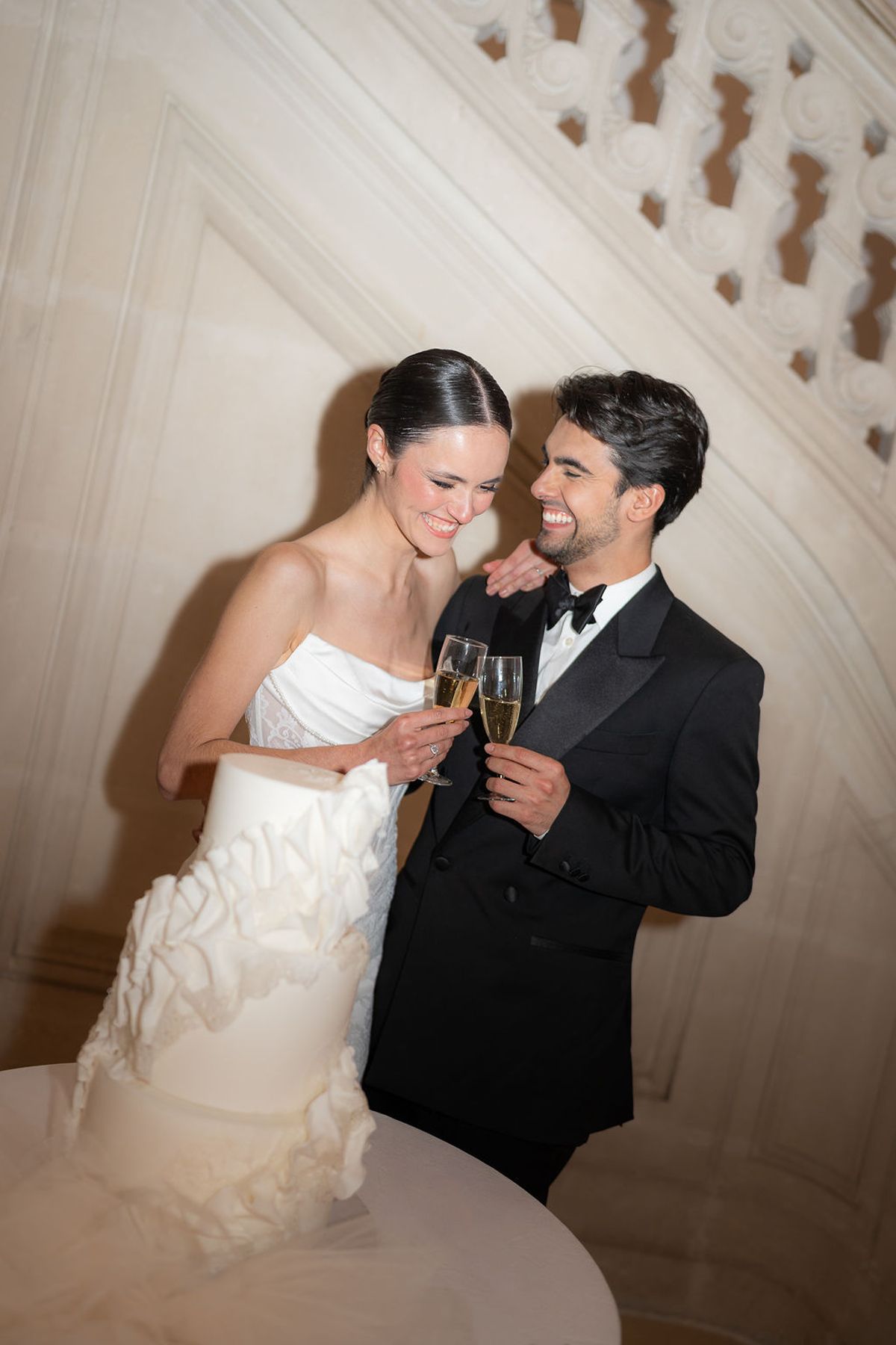 Two dancers touching coupes of champagne beside a ruffled cake