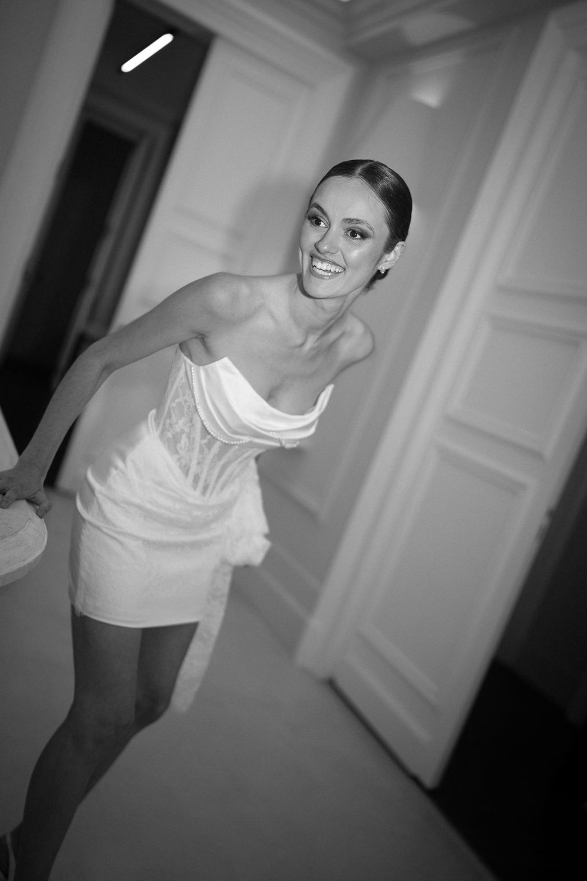 Black and white frame of a dancer stepping through a doorway in a short structured dress