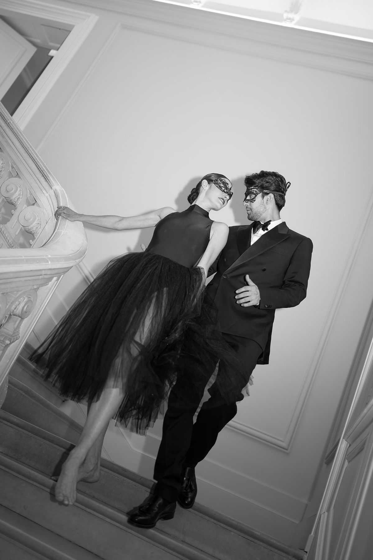 Black and white frame of two dancers mid-step, one in a tulle skirt, one in black tie