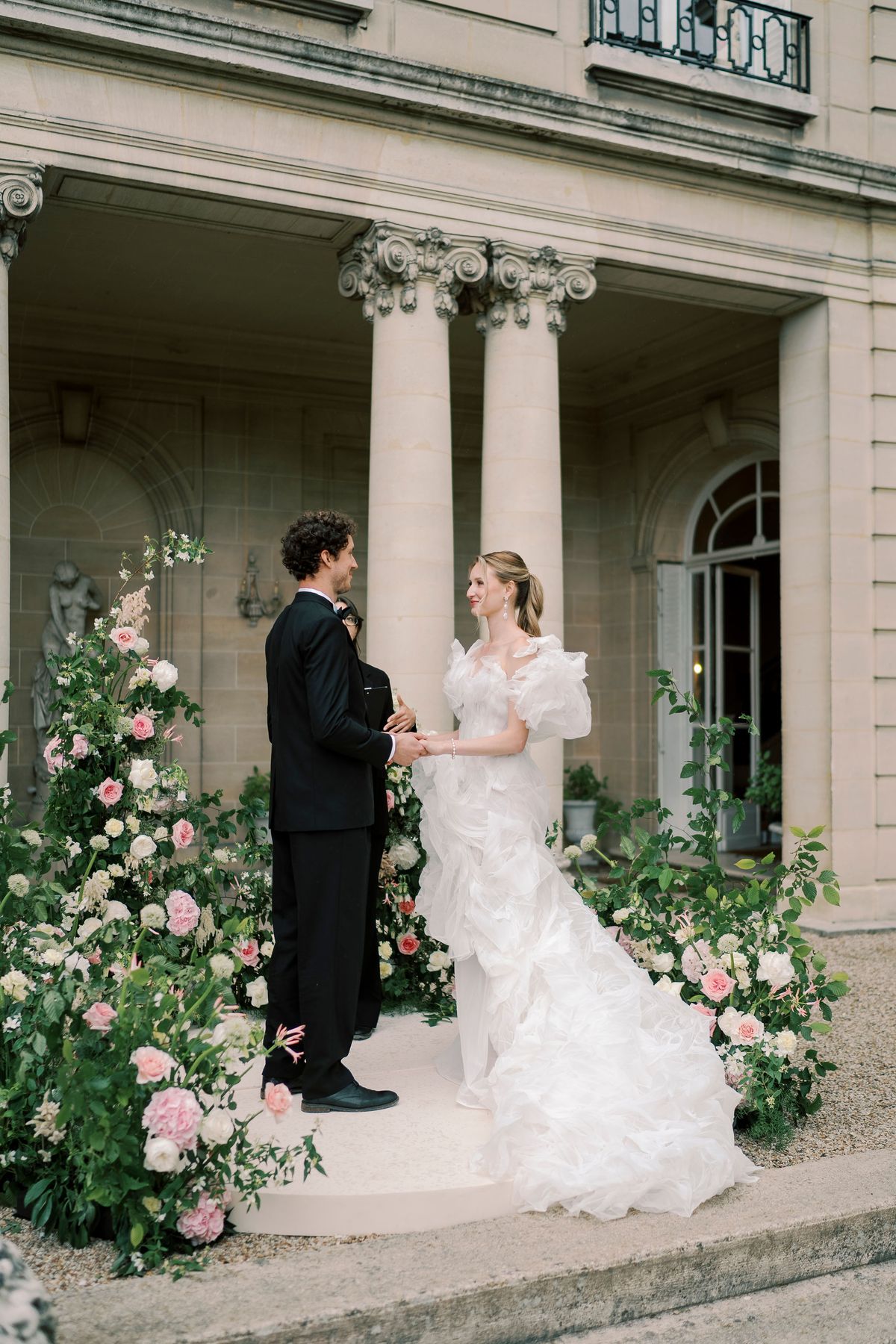 Amélie and Lucien holding hands on the circular platform, garden roses on either side