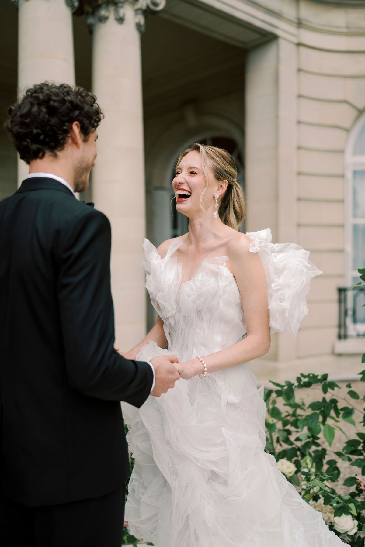 Amélie laughing as she holds Lucien's hands in front of the stone columns