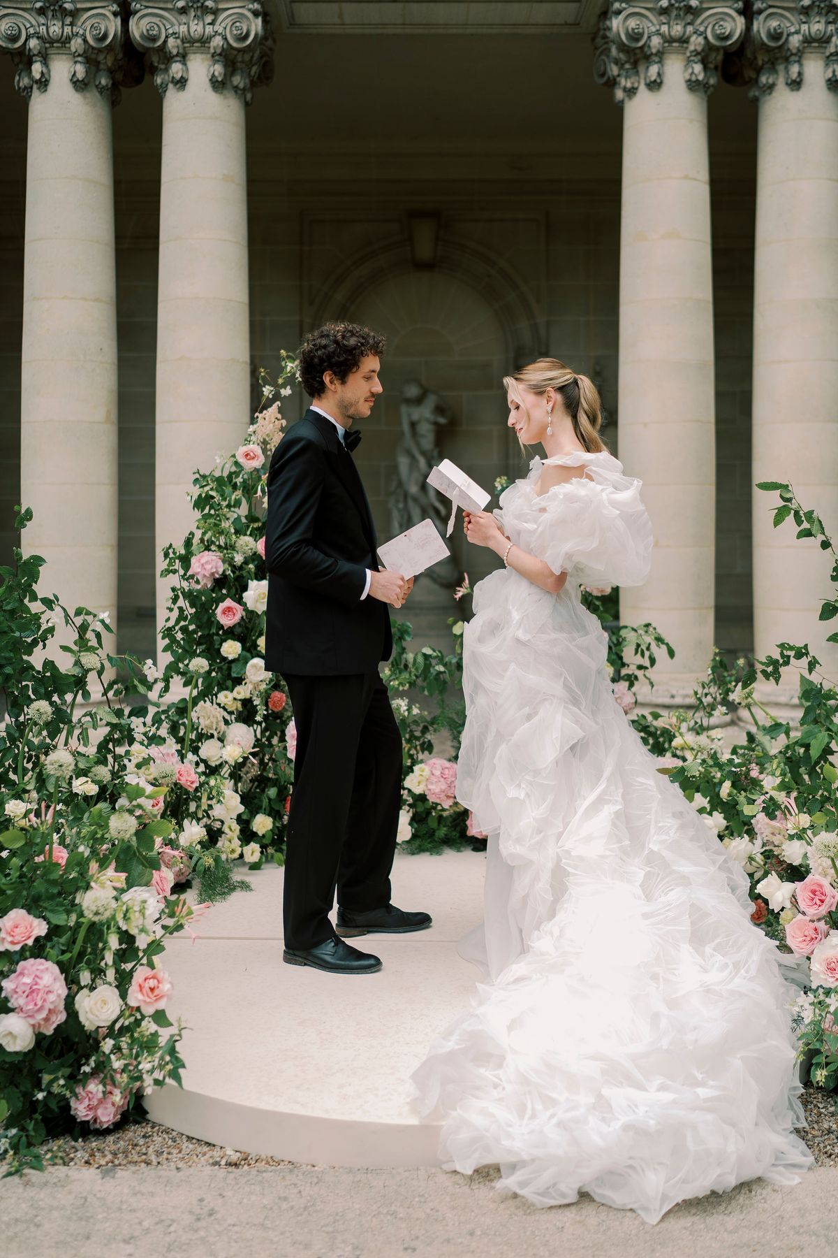 Amélie and Lucien holding vow cards on the flower-framed circular platform