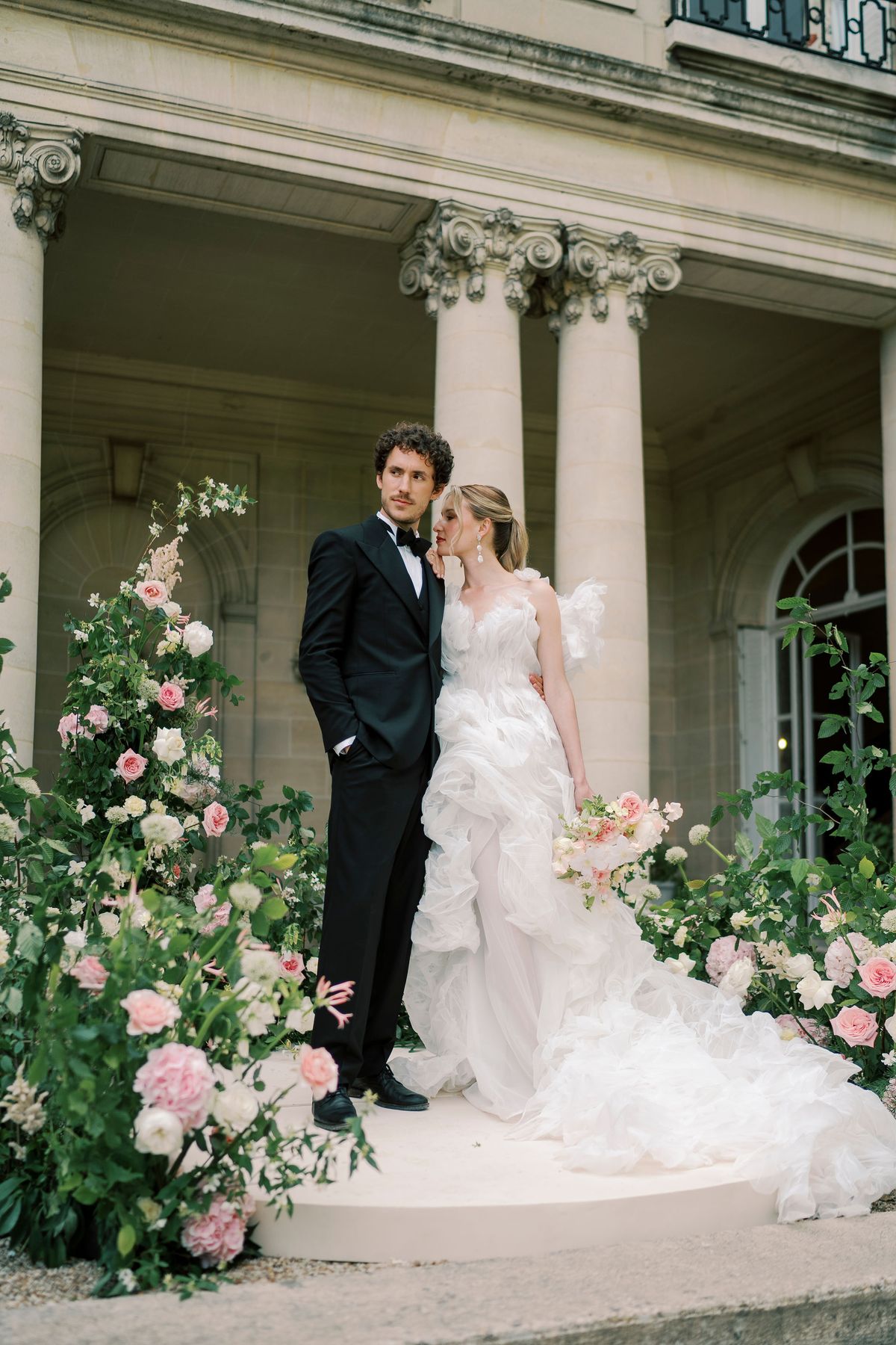 Amélie resting her head on Lucien's shoulder beside the peristyle columns