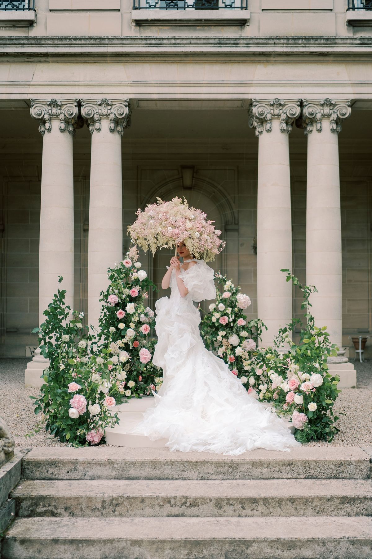 Amélie holding her bouquet up to her face on the circular platform, roses either side