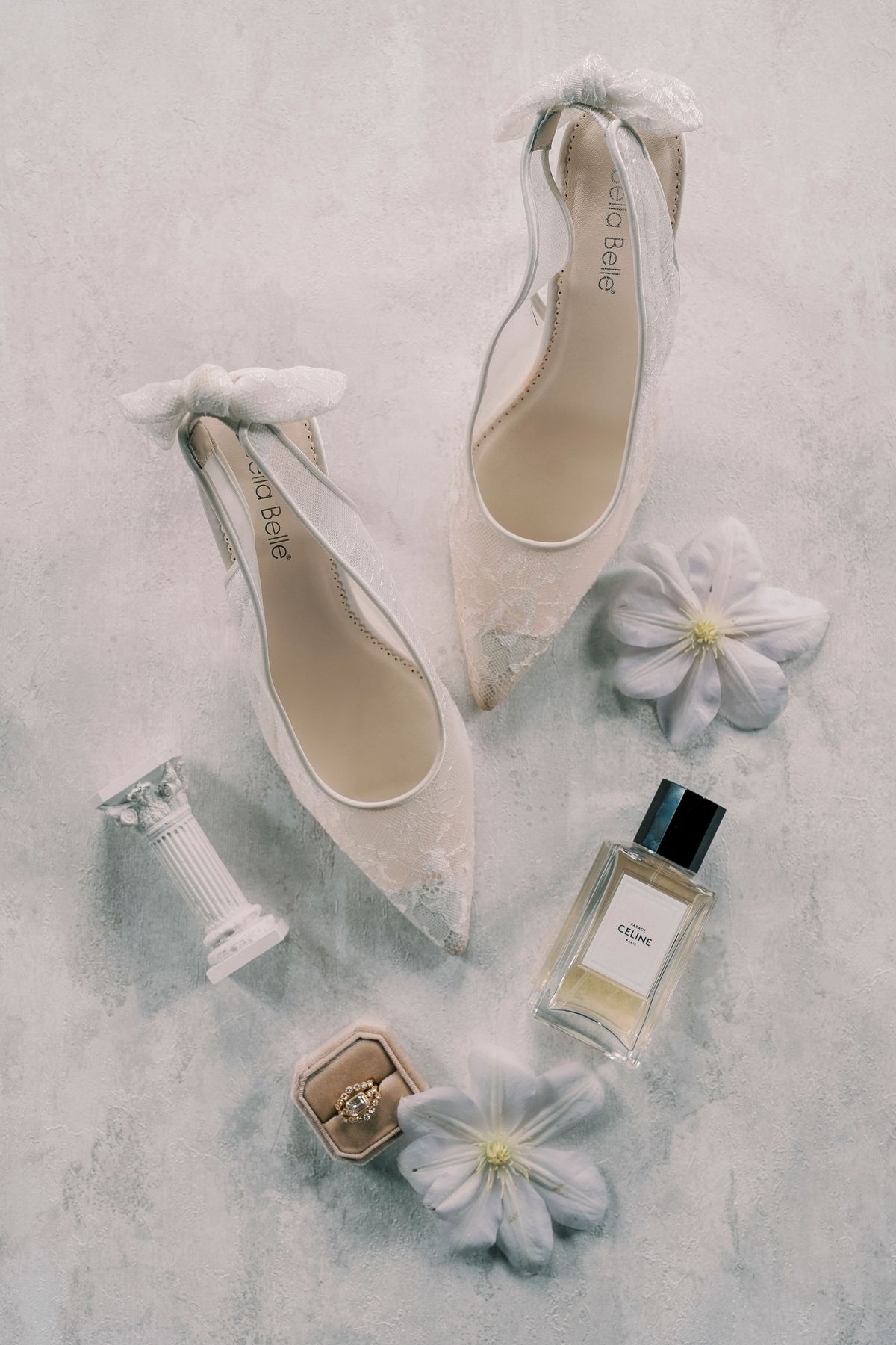 Flat lay of bridal shoes with bows, a perfume bottle, a ring box and white flowers