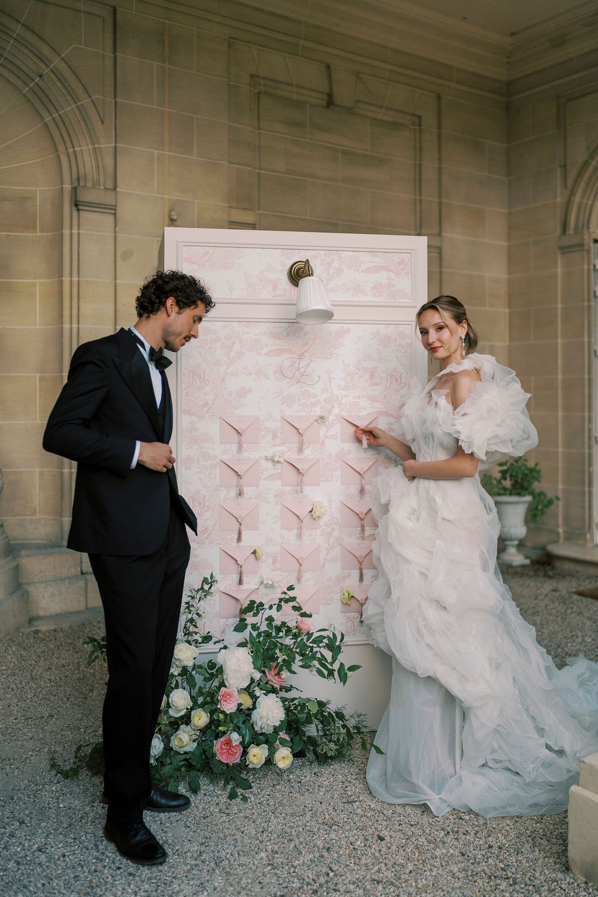 Amélie and Lucien beside the pink seating chart panel inside the stone peristyle