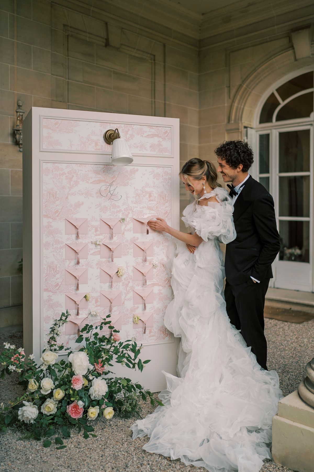 Amélie and Lucien reading names on the toile de Jouy seating chart, roses at its foot
