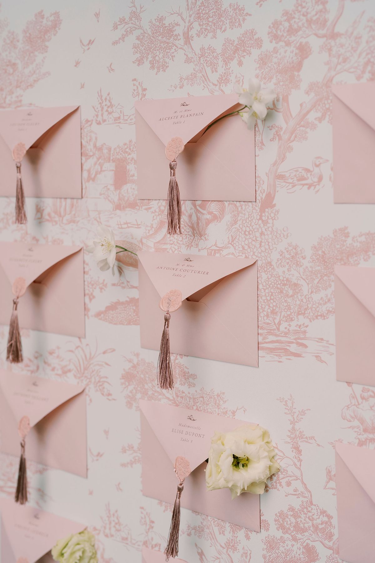 Pink envelopes with wax seals and tassels on blush toile de Jouy wallpaper