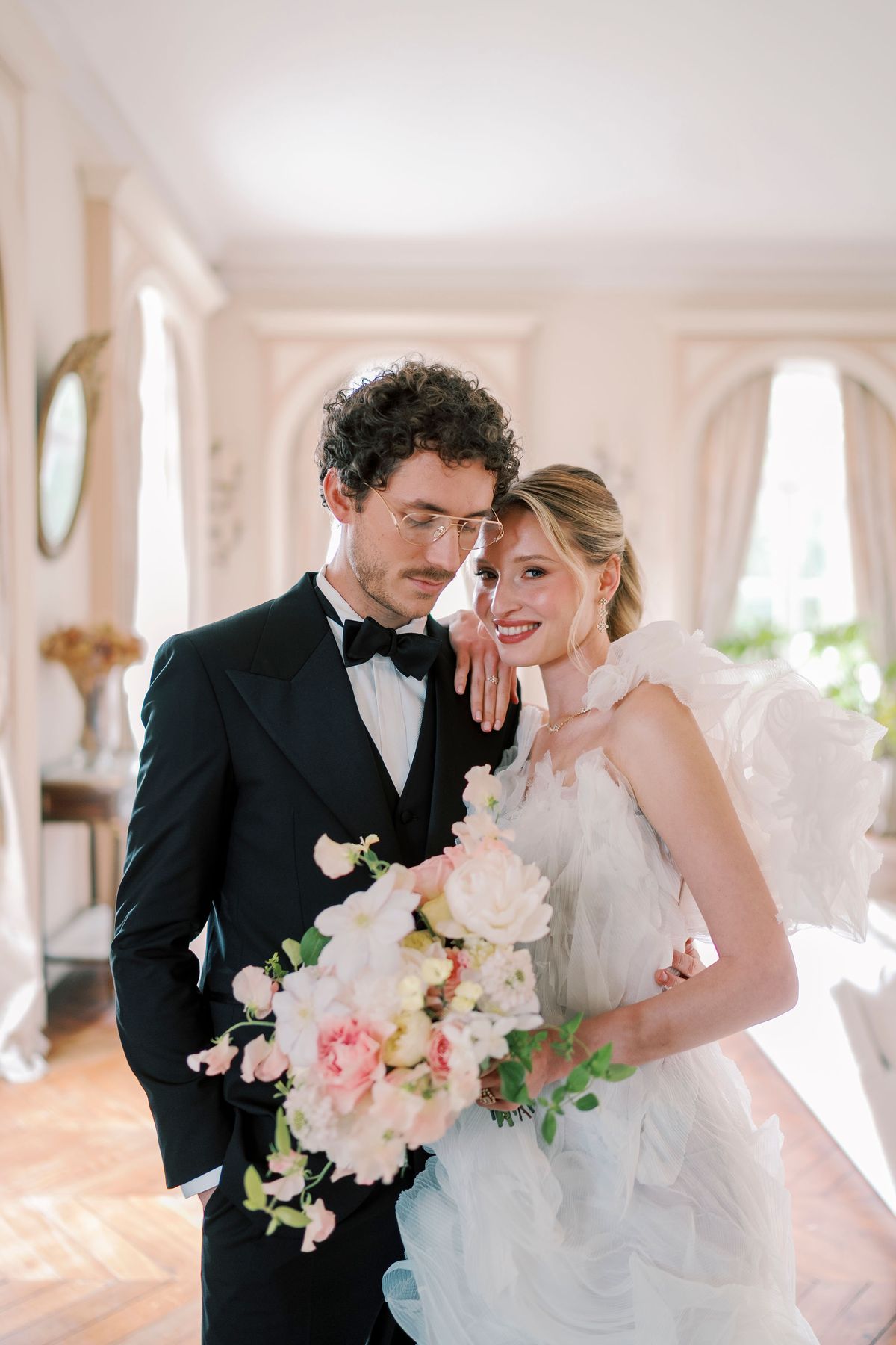 Amélie and Lucien smiling together in a salon, her head on his shoulder, bouquet in hand