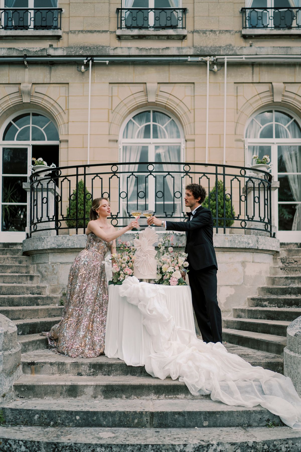 Amélie and Lucien raising glasses across the cake table on the terrace steps